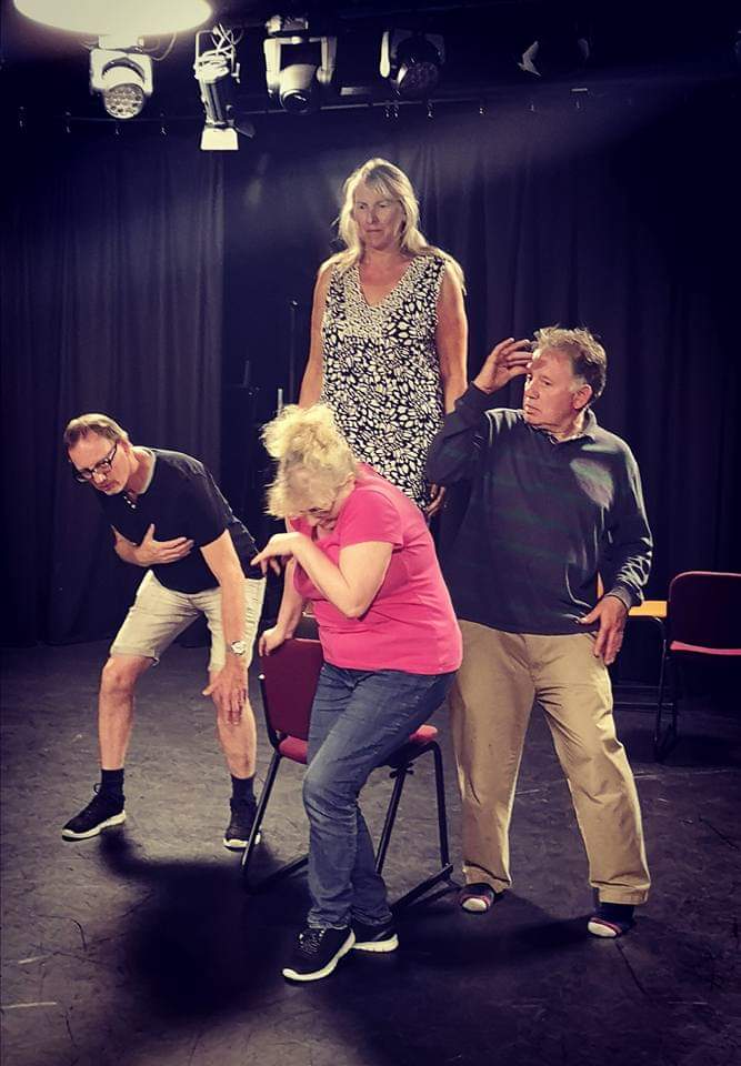 Movement workshop Tracey raised up on chair as other bow and quiver below her