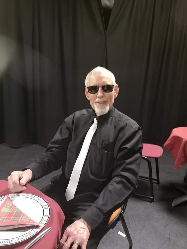 Sid in gangster outfit featuring white silk tie and black shirt. Sid is wearing dark tinted glasses and is smiling