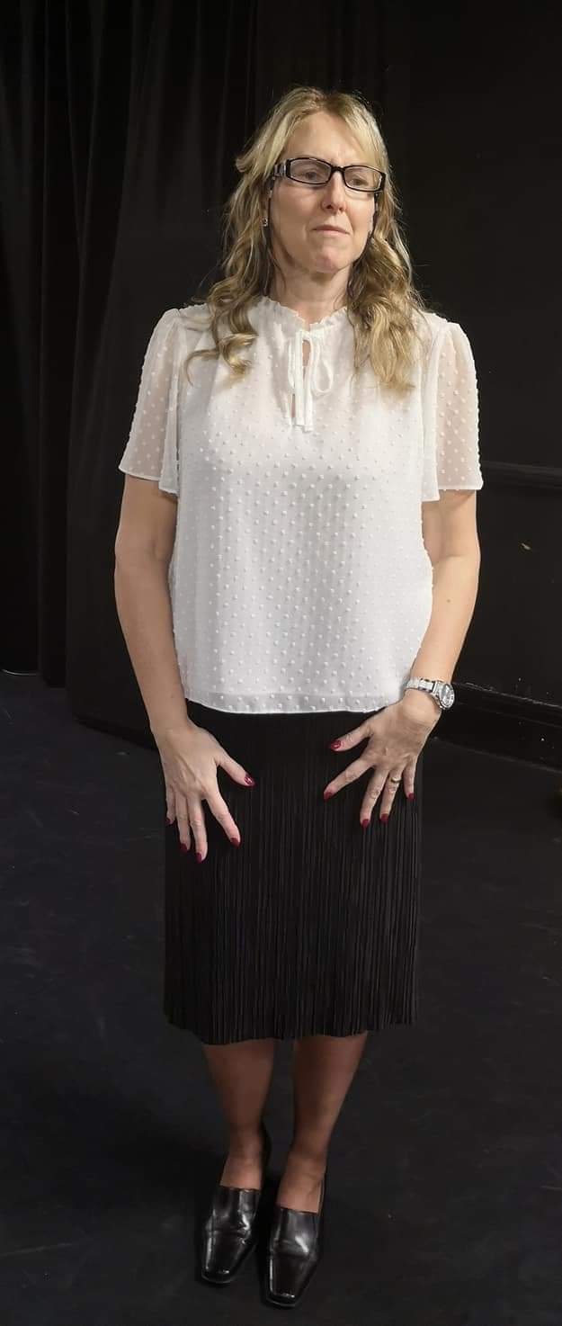 Tracey wearing white blouse has blond hair and is wearing glasses; looking very official