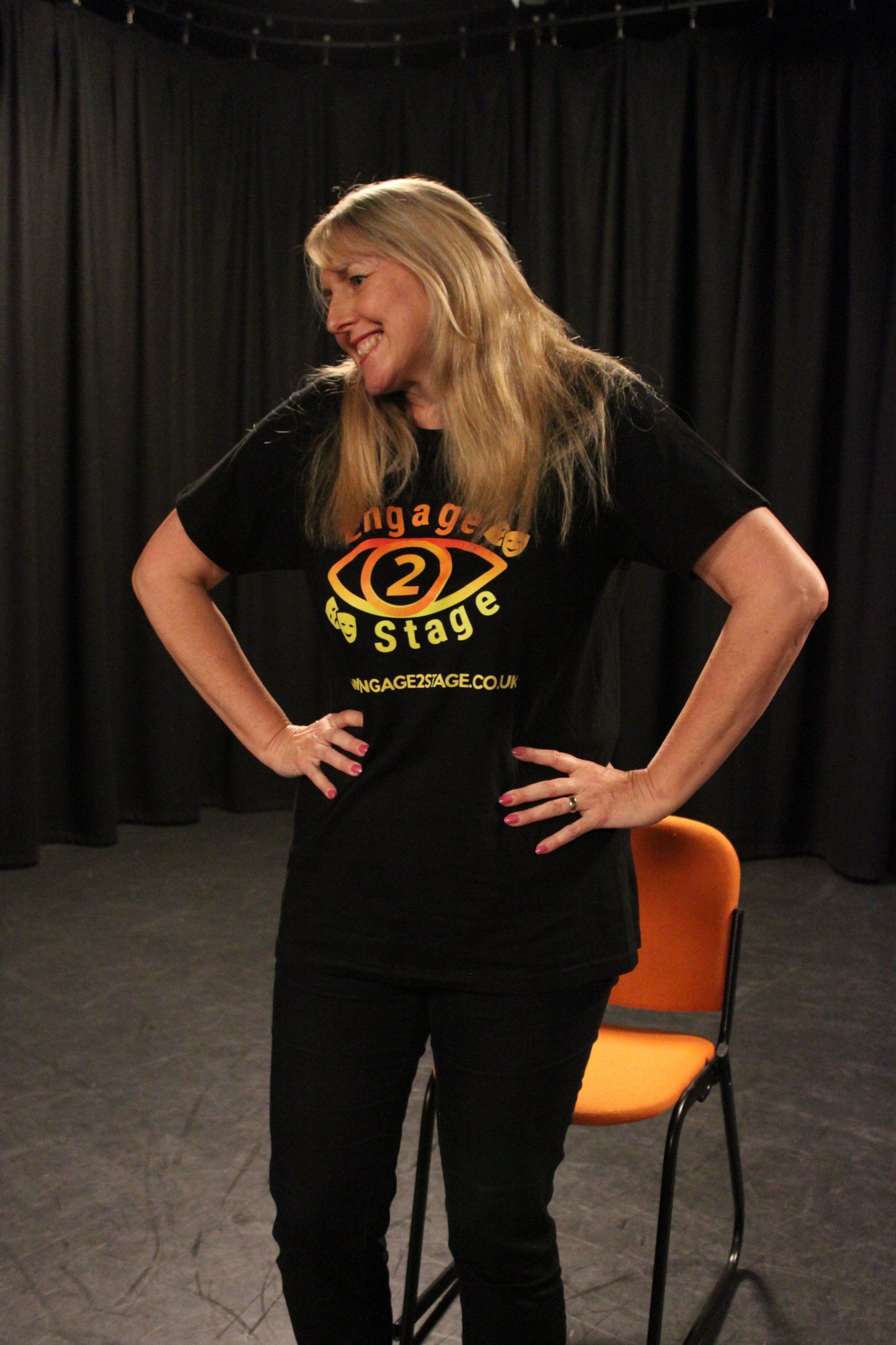 Tracey in black box studio with hands on hips smiling