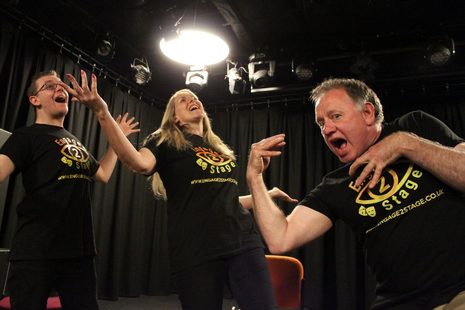 3 people in box studio making arm movements pulling expressive faces.