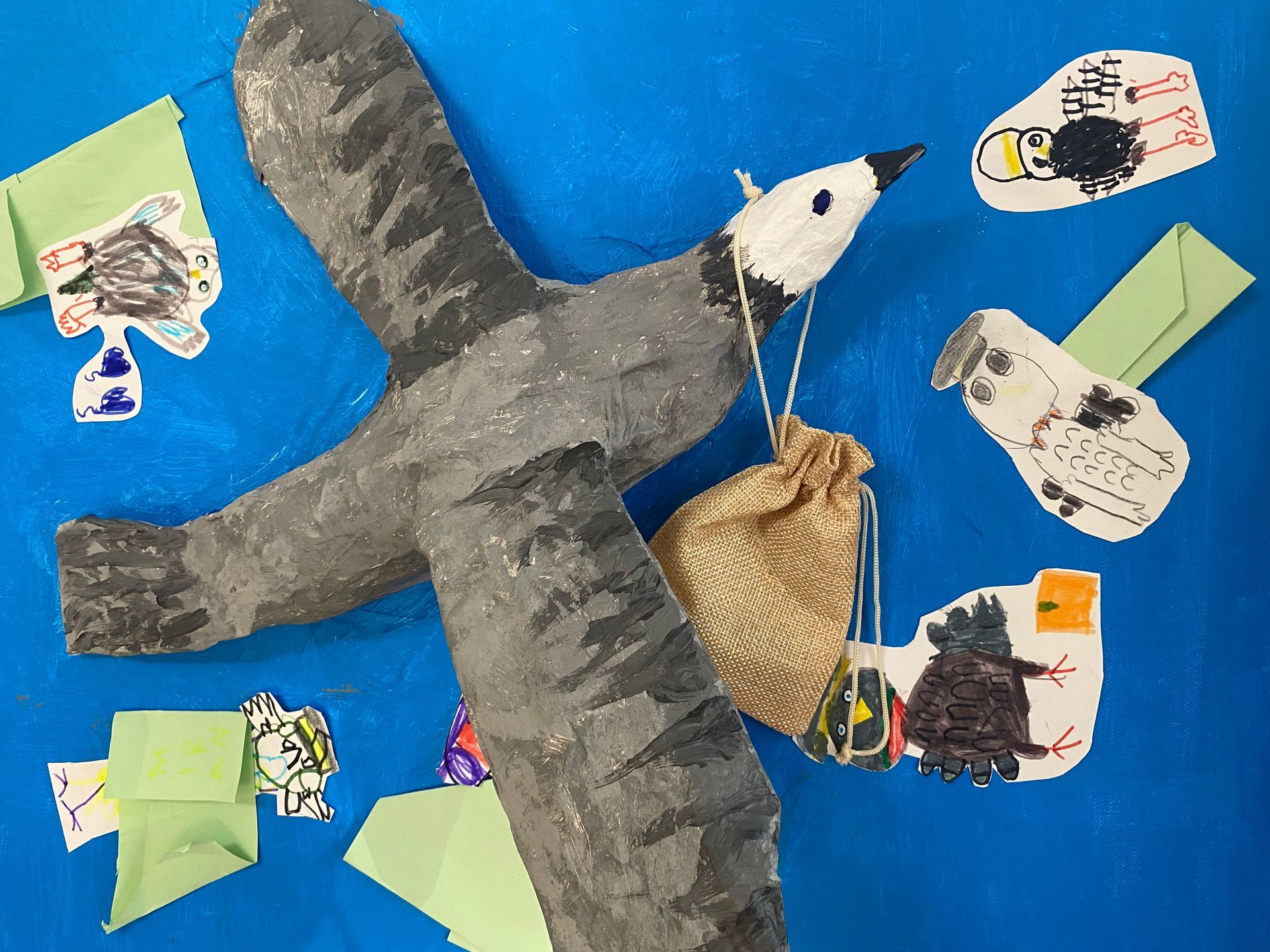 Papiervogelcollage auf blauem Hintergrund mit grauen Flügeln, weißem Kopf und kleinen dekorativen Ausschnitten drumherum