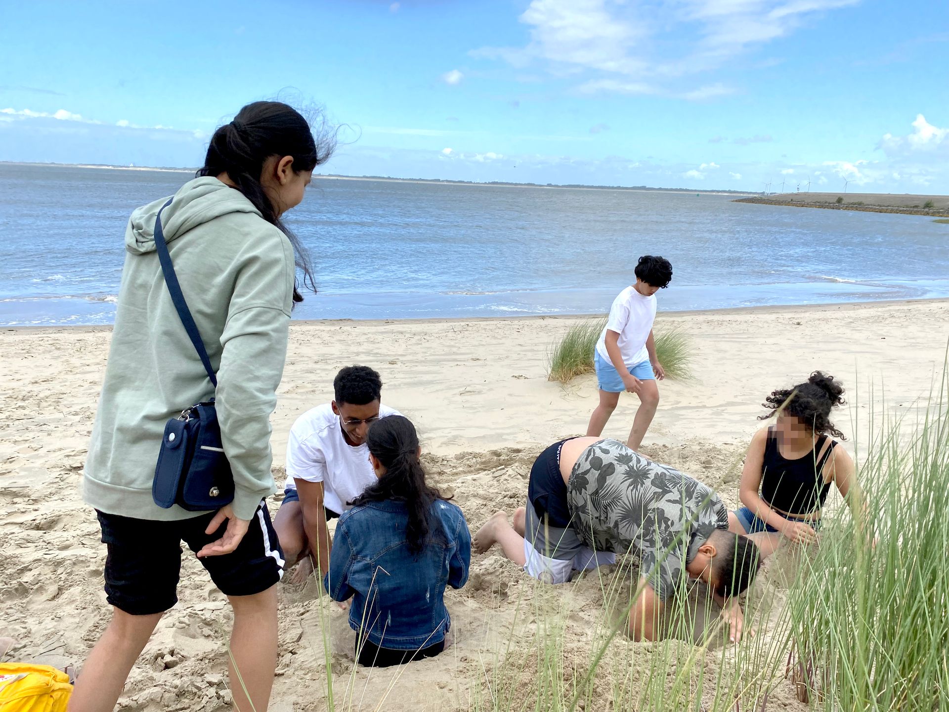 Menschen an einem Sandstrand nahe dem Wasser, die unter blauem Himmel beieinander sitzen und hocken.