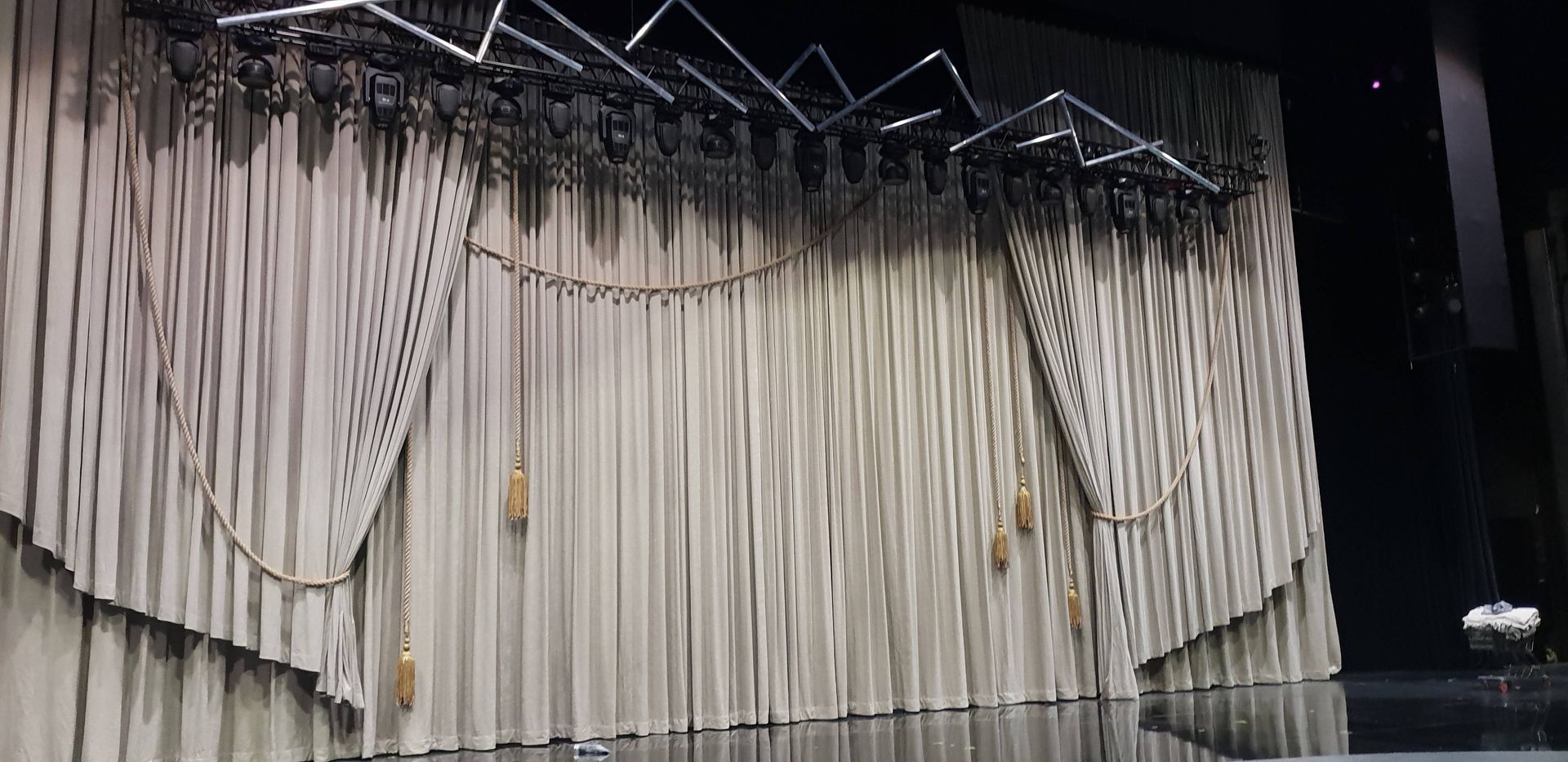 Theaterbühne mit beigefarbenen Vorhängen, dekorativer Beleuchtung darüber und Quasten.