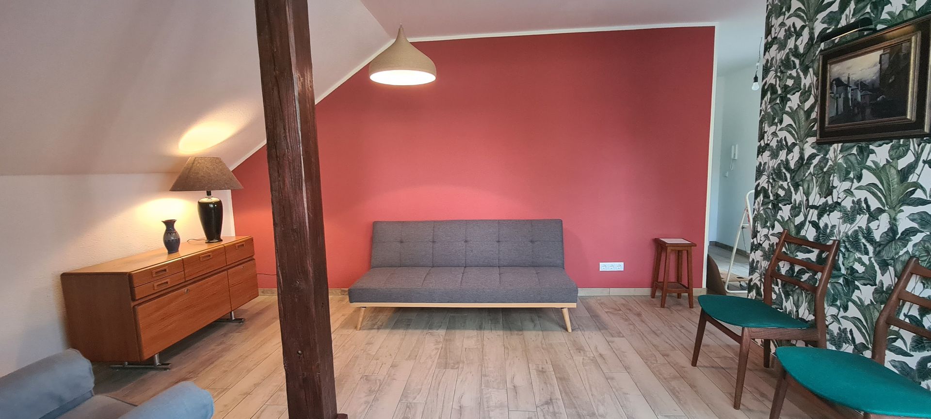 Wohnzimmer mit roter Wand, grauem Sofa, Holzmöbeln und gemusterter Tapete.