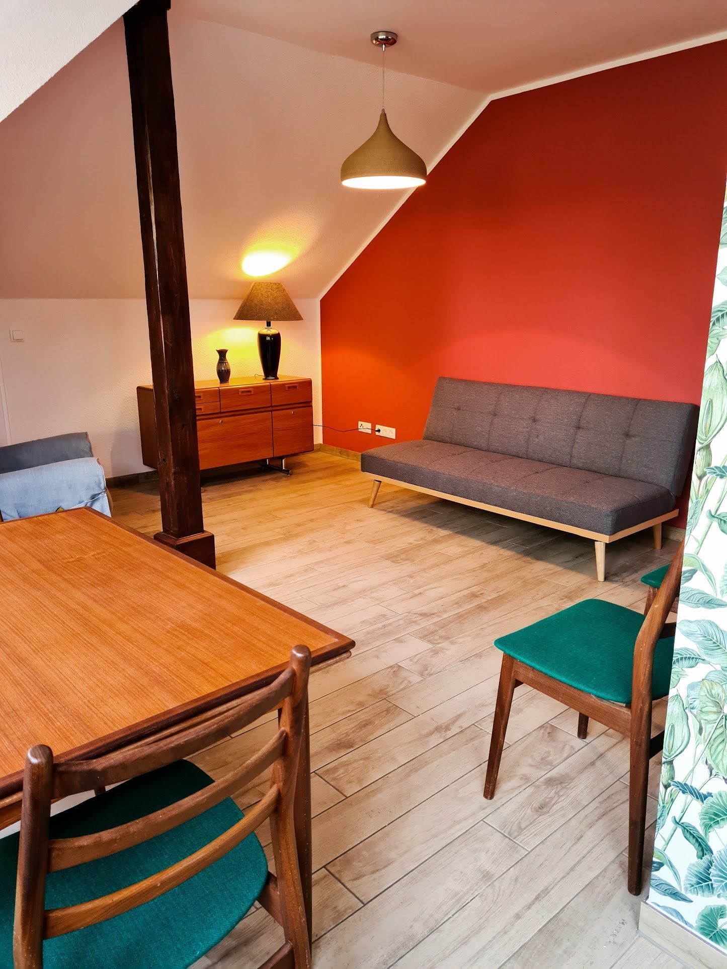 Wohnzimmer mit roter Wand, grauem Sofa, Holzmöbeln und hellem Holzboden.