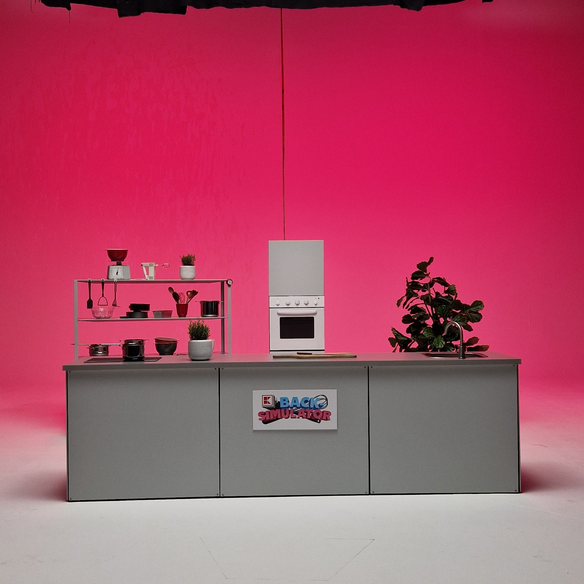 Miniaturküchenset mit rosa Hintergrund, grauer Arbeitsplatte, Herd, Regalen mit Gegenständen und einer Pflanze.