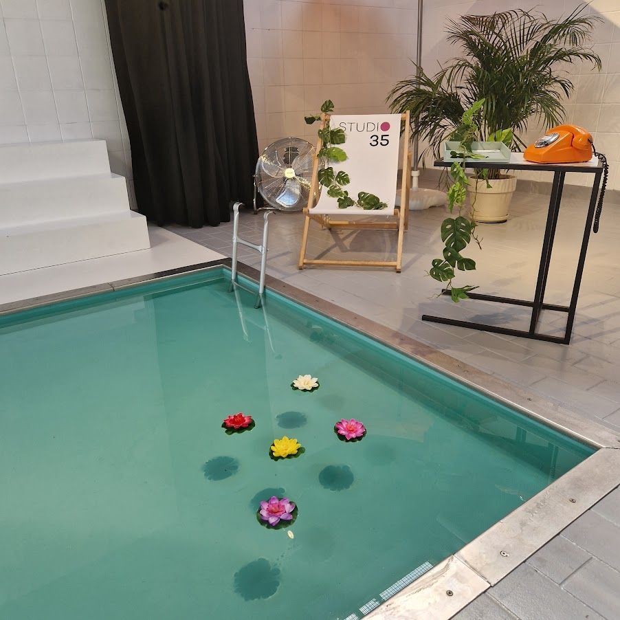 Kleiner Pool mit schwimmenden Blumen, einem Schild, einem Ventilator und Topfpflanzen.