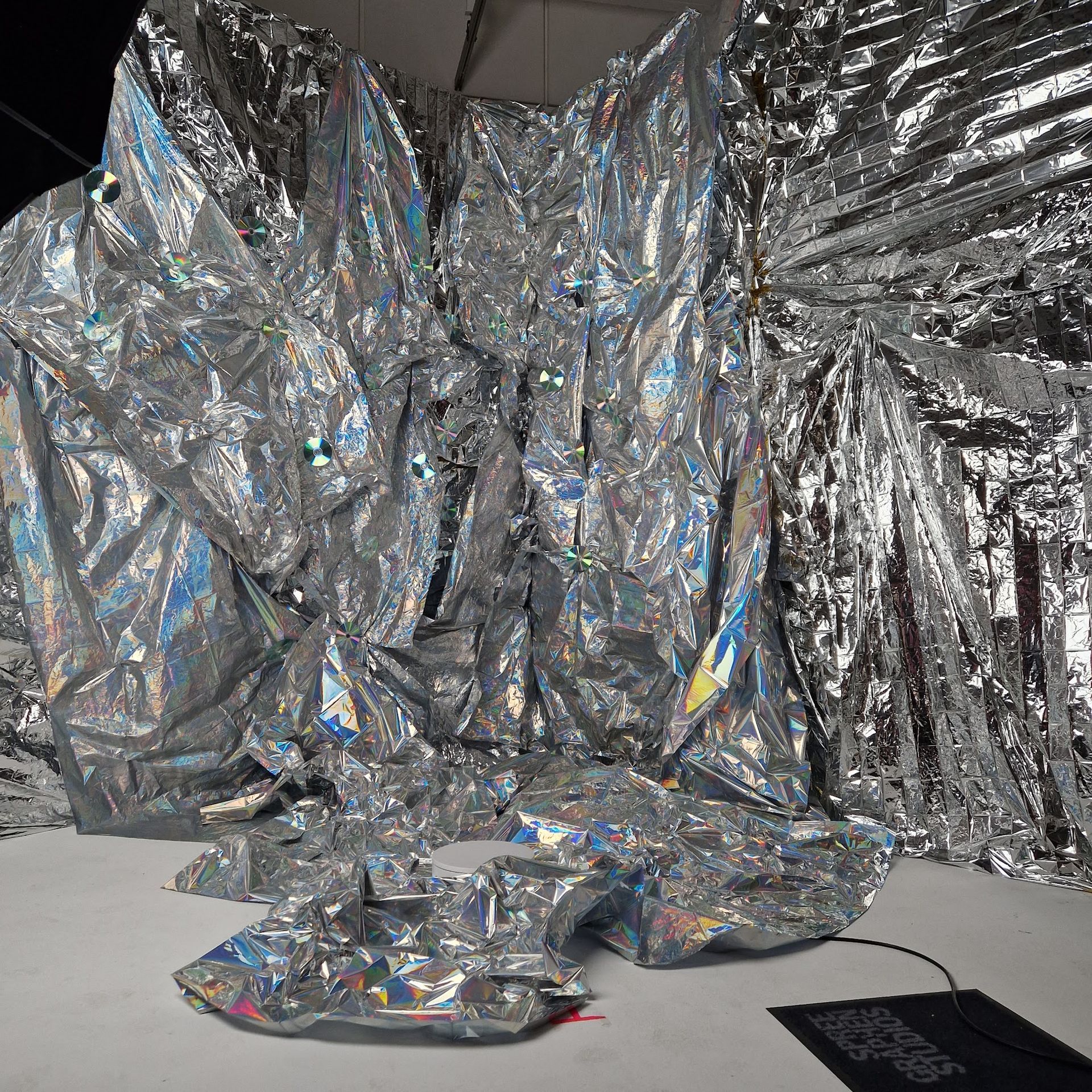 Silbernes, zerknittertes, reflektierendes Material bildet eine höhlenartige Struktur in einem Raum mit weißem Boden.