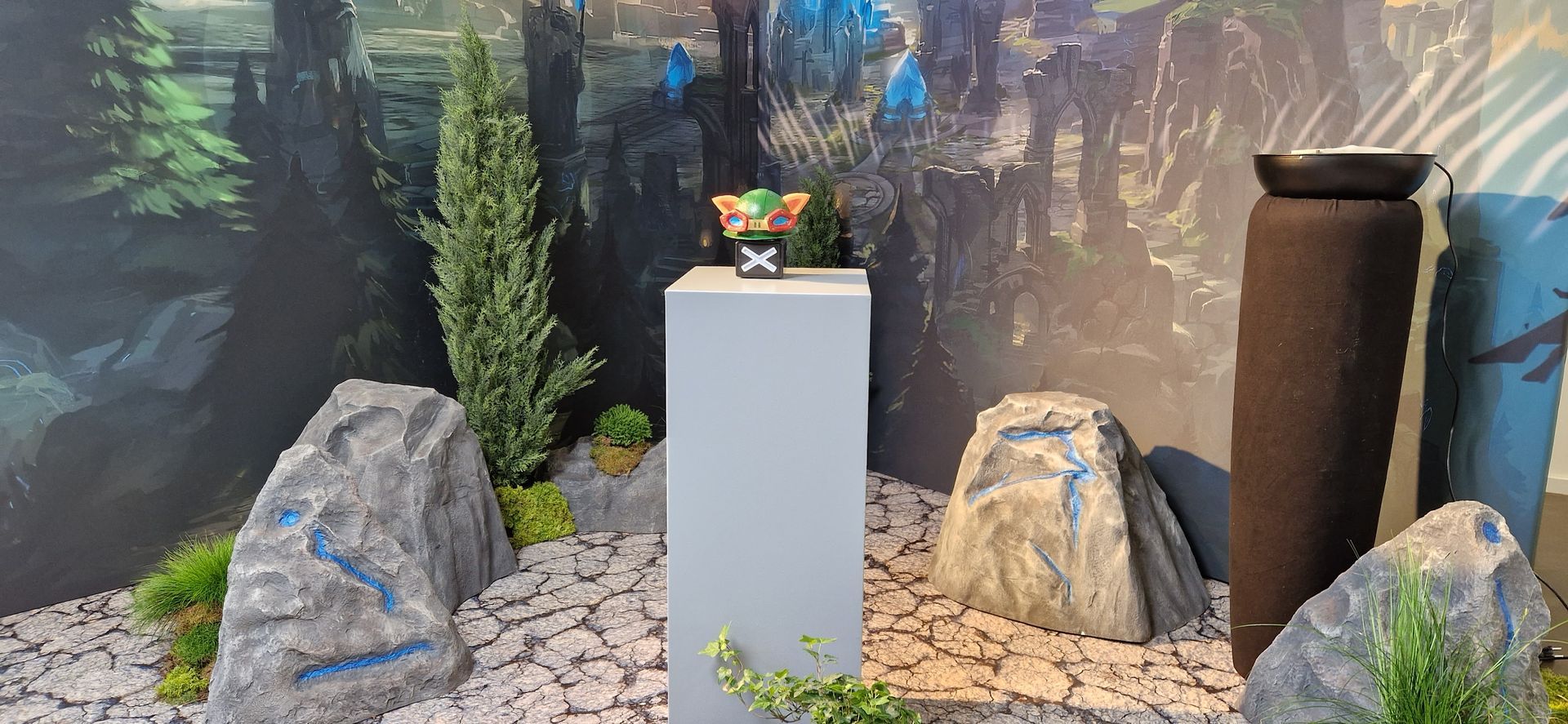 Eine Vitrine zeigt eine kleine Figur auf einem Sockel, eingebettet in ein naturalistisches Diorama mit Felsen und Laubwerk.