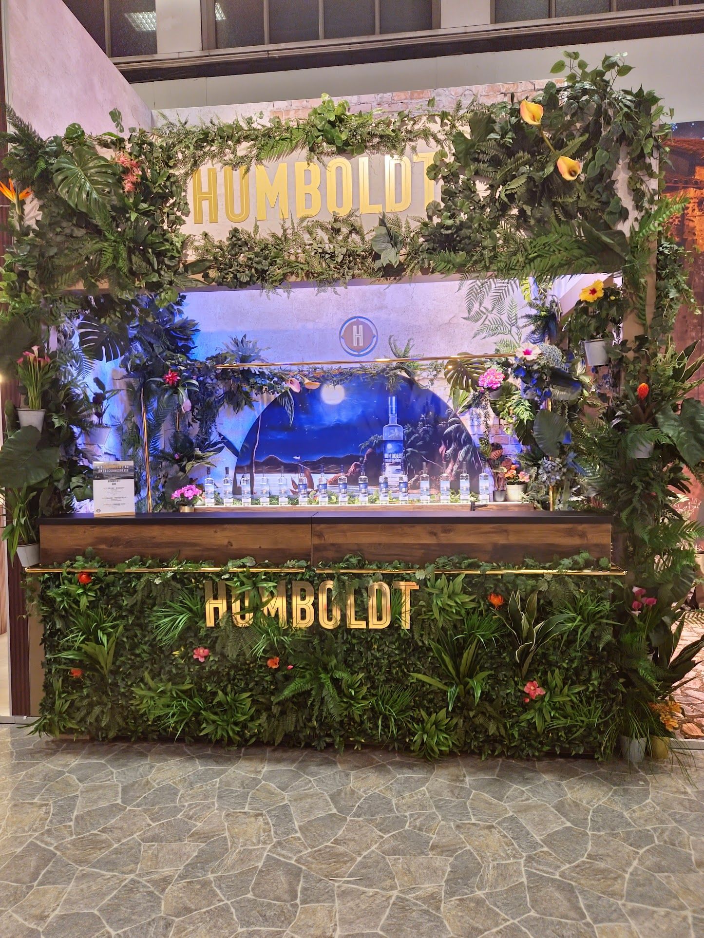 Ein Bardisplay mit „HUMBOLDT“ in goldenen Buchstaben, üppigen grünen Pflanzen und einer Hintergrundszene.