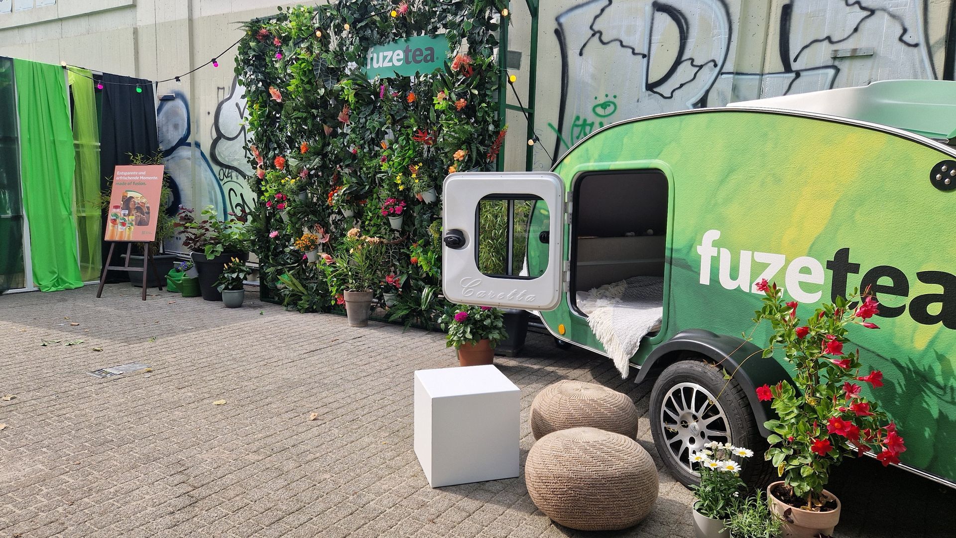 Werbedisplay von Fuze Tea mit einem grünen Wohnwagen, einer Blumenwand und Sitzgelegenheiten.