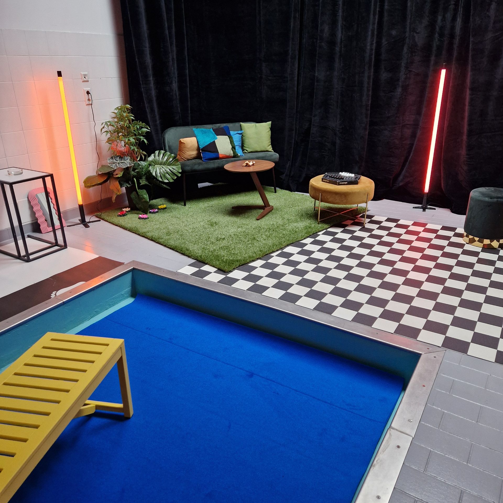 Innenszene mit Pool, Sitzbereich mit grünem Teppich, schwarzem Hintergrund und bunten Akzenten.