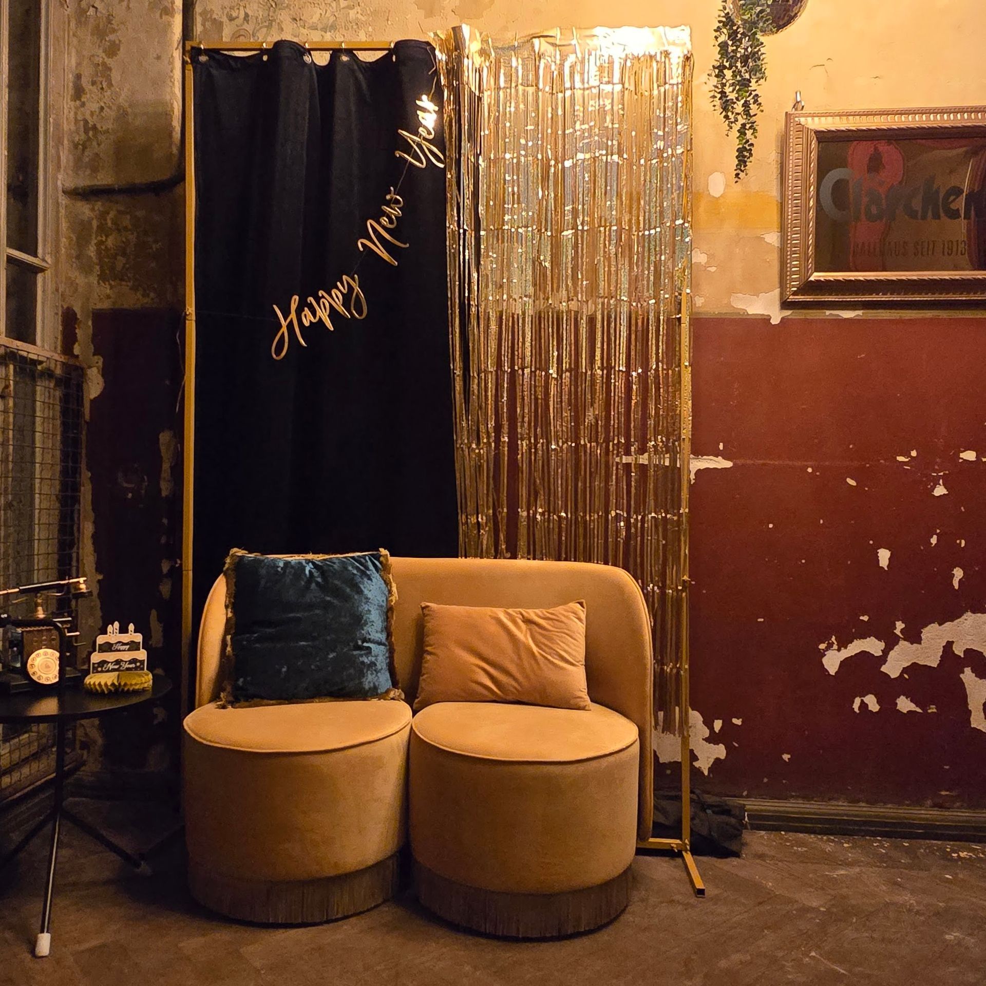 Lounge-Bereich in Gold und Schwarz für Silvester. Samtstühle, Vorhänge und eine Kulisse mit goldenen Fransen in einem alten Gebäude.