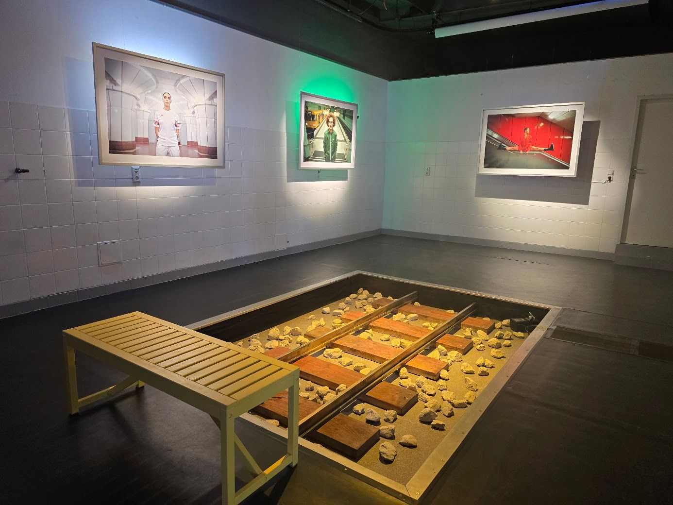 Galerie mit Kunstwerken, einer Bank und einer versenkten Ausstellung von Eisenbahnschienen und Trümmern.