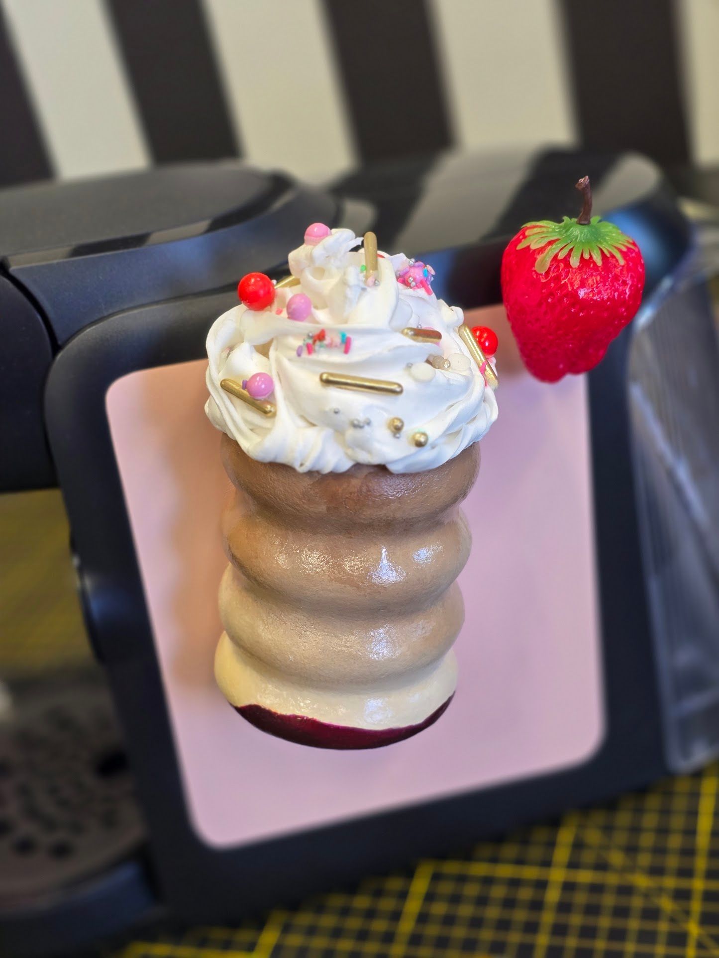 Ein geschichtetes Gebäck mit Schlagsahne und Streuseln, daneben eine Erdbeere, auf einem rosa Quadrat, auf einem schwarzen Gerät.