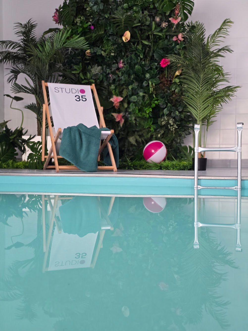 Szene am Pool: Liegestuhl mit Handtuch, Pool, tropische Pflanzen, ein Strandball.