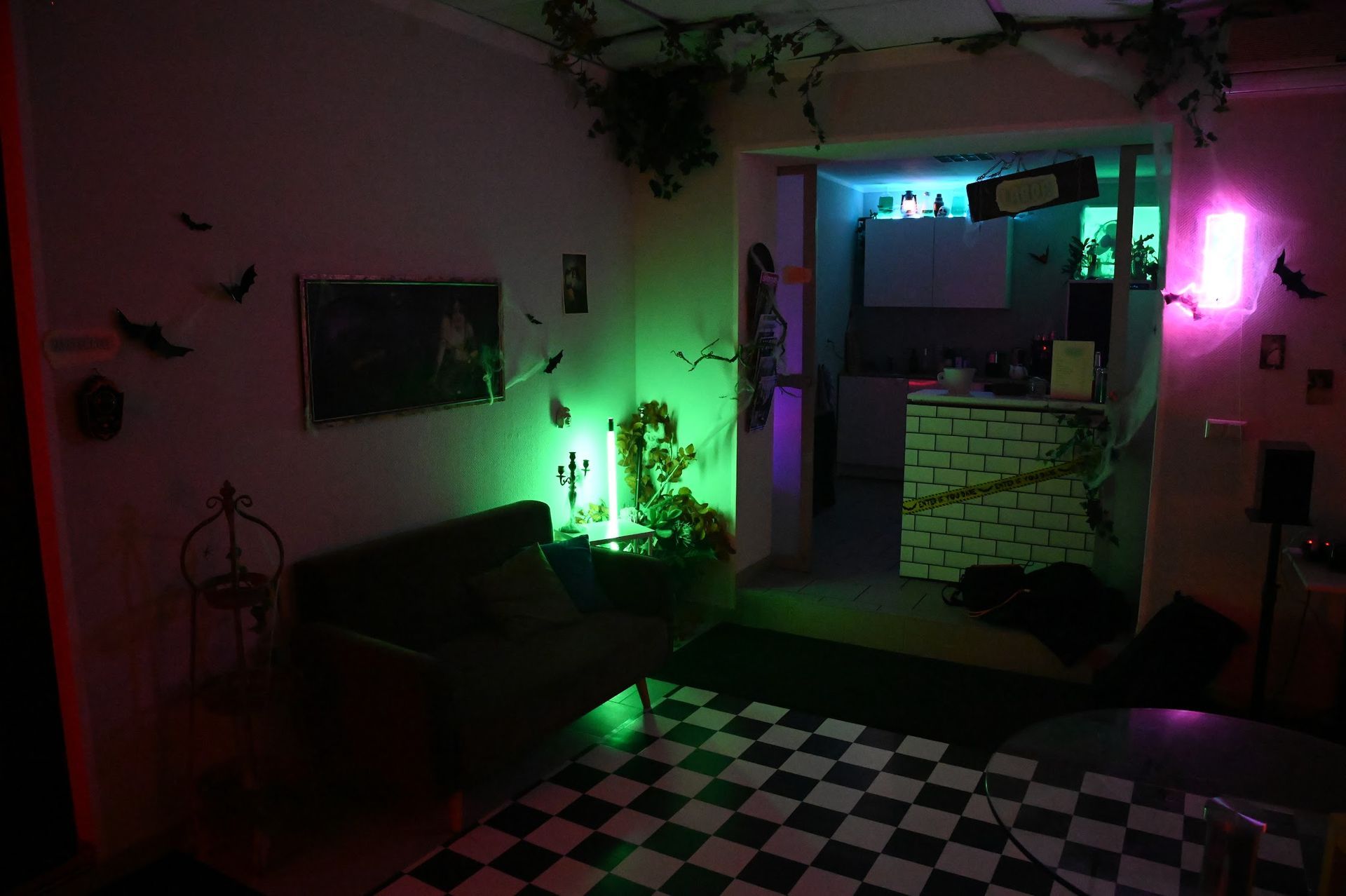 Ein Zimmer, das für Halloween mit grünen und rosa Lichtern, Fledermäusen und einem karierten Boden dekoriert ist.