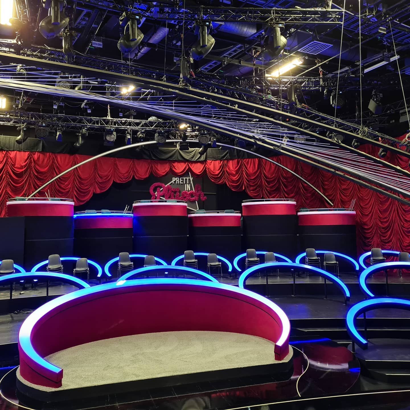 Spielshow-Set mit geschwungenen Sitzreihen, beleuchteten Bühnen und rotem Samtvorhang als Hintergrund.