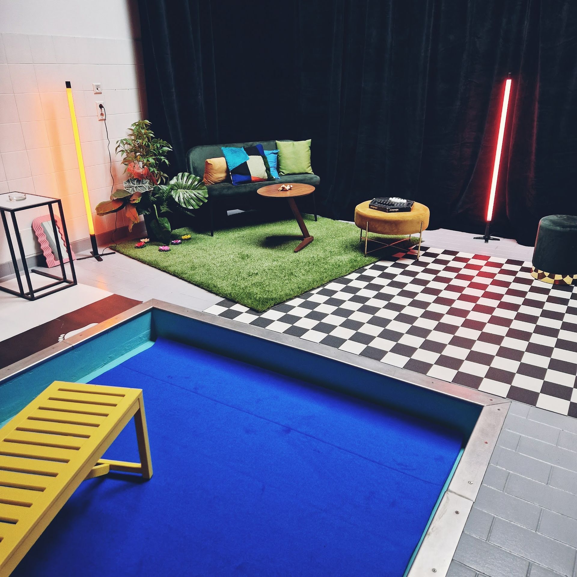 Zimmer mit Pool, Sitzecke, schwarz-weiß kariertem Boden und Neonlichtern.
