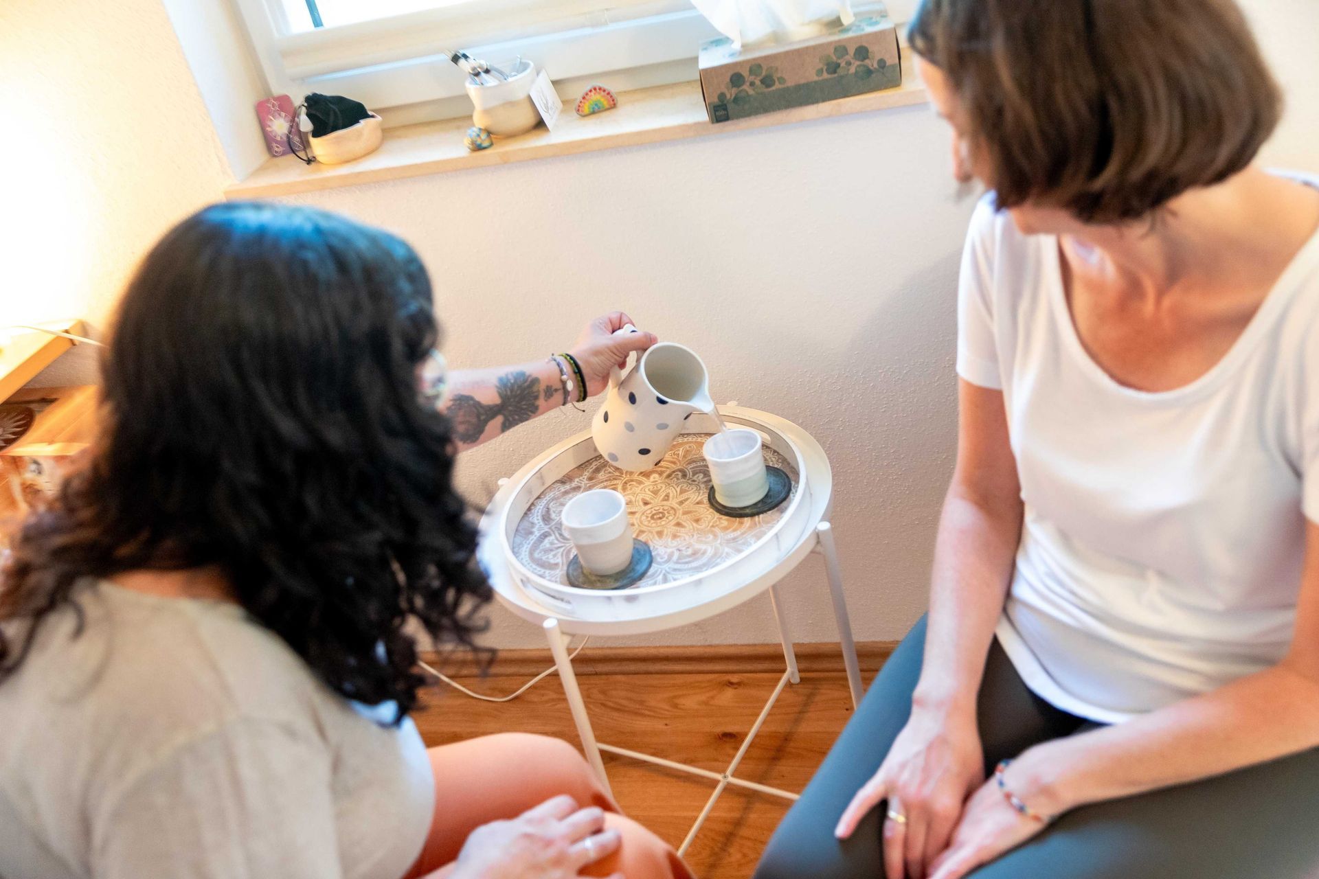Nina Stepanek im Gespräch mit Klientin, beide Frauen sprechen miteinander und Nina schenkt Wasser in eine Tasse ein