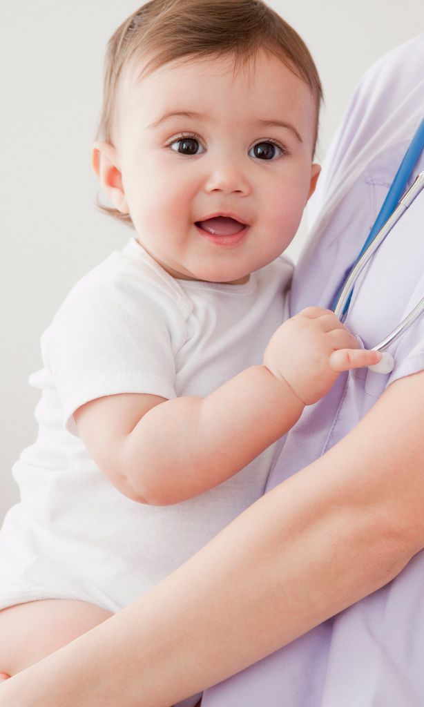 Ein Baby in einem weißen Strampler wird von einer medizinischen Fachkraft gehalten, die eine hellviolette Uniform und ein Stethoskop trägt.
