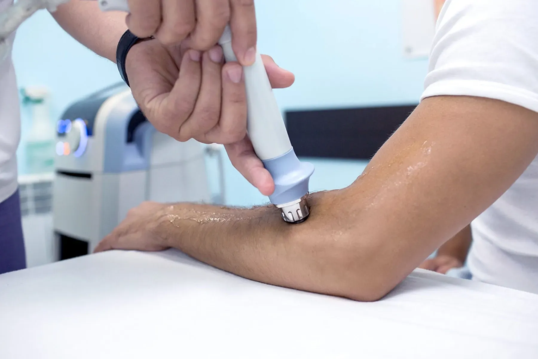 Ein Physiotherapeut verwendet in einer klinischen Umgebung einen Ultraschalltherapie-Stab am Arm eines Patienten.