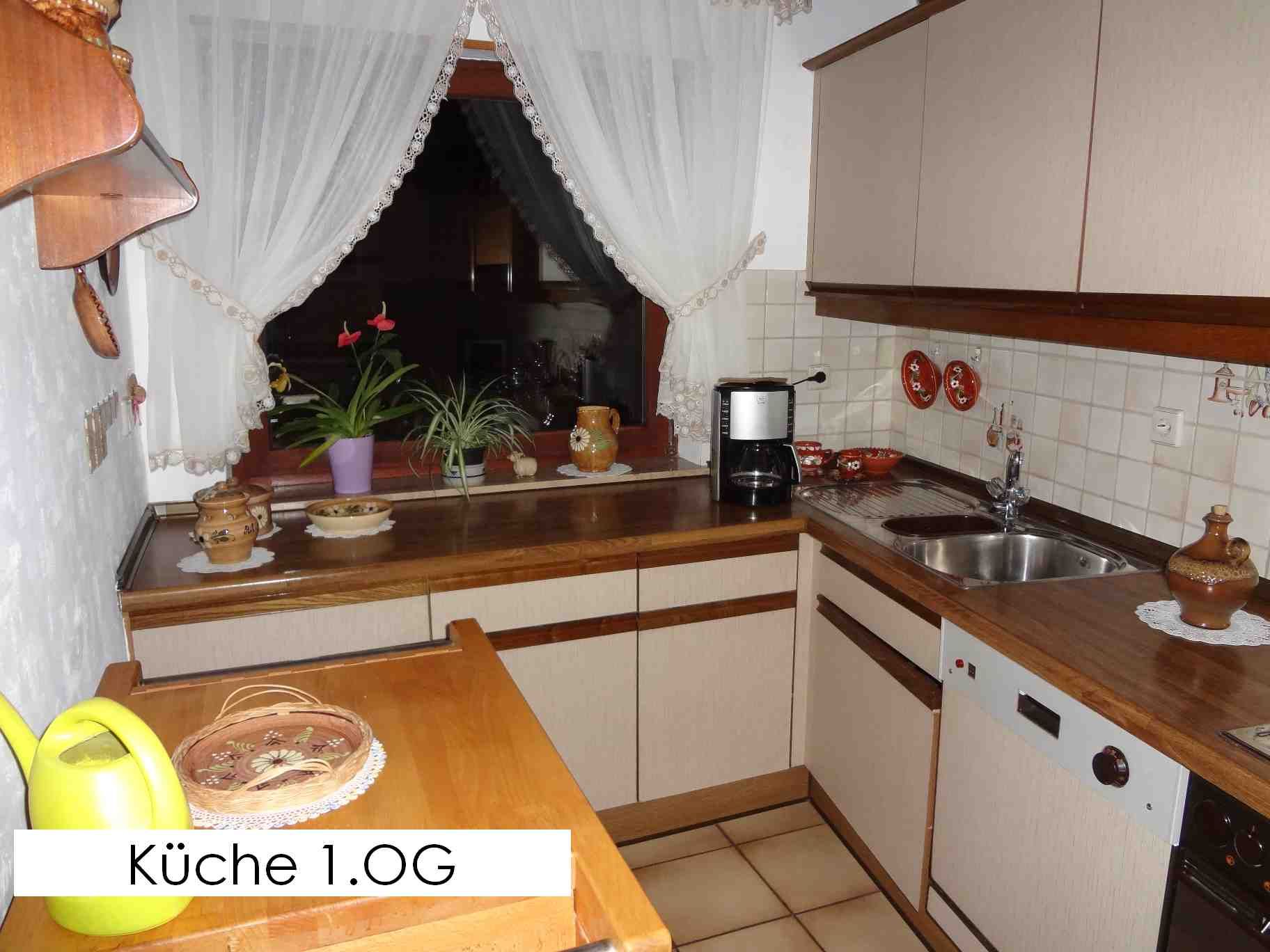 Küche mit hellen Schränken, Arbeitsplatten aus Holz und einem Fenster mit Pflanzen und Vorhängen.