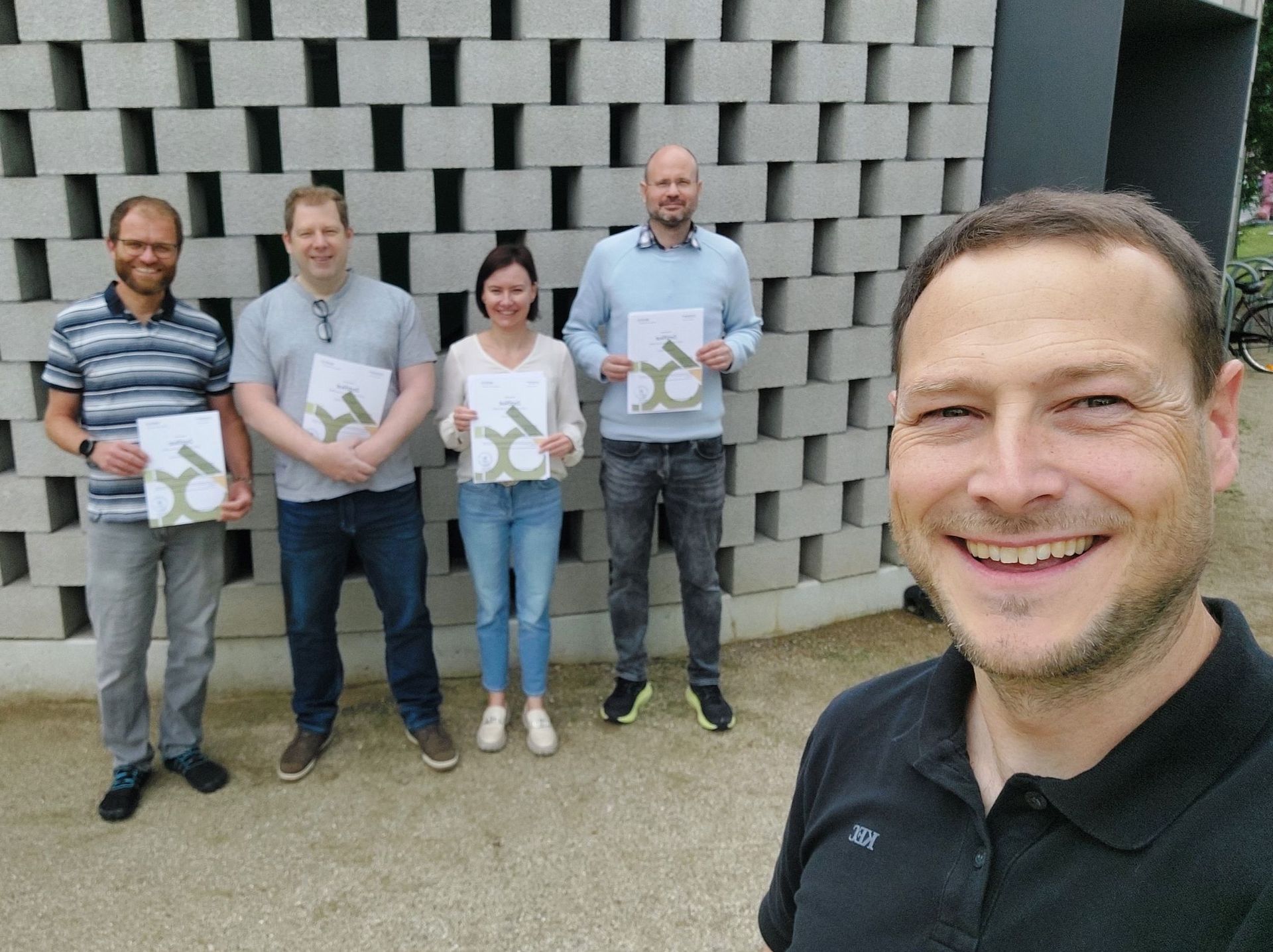 Manuel Kugler und erfolgreiche Teilnehmende mit Ihren Zertifikaten stehen vor einer Wand
