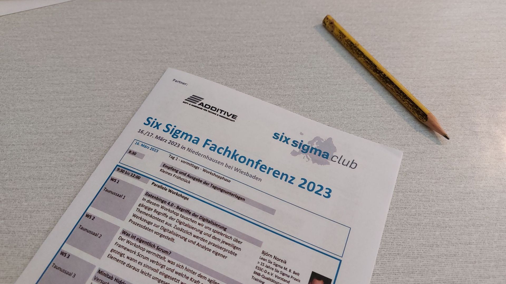 Das Programm der Six Sigma Fachkonferenz 2023 und ein Bleistift liegen auf dem Schreibtisch