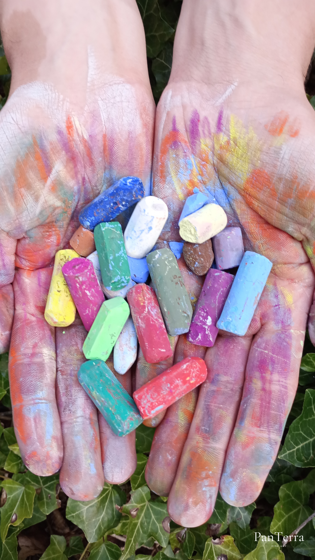 Die Hände sind zu einer Schale geformt und halten bunte Kreidestücke, die Handflächen sind mit Kreidestaub bedeckt.