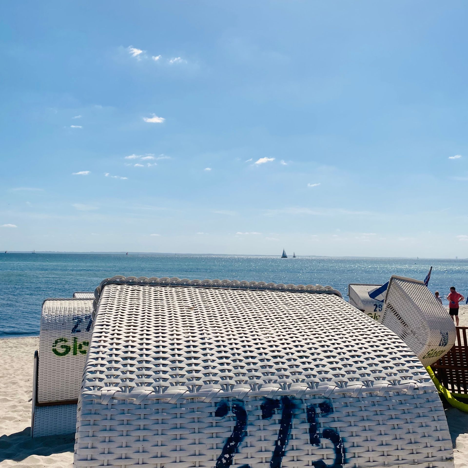 Ein mit 275 gekennzeichneter Strandstuhl steht auf einem Sandstrand mit Blick auf den Ozean unter einem klaren blauen Himmel.
