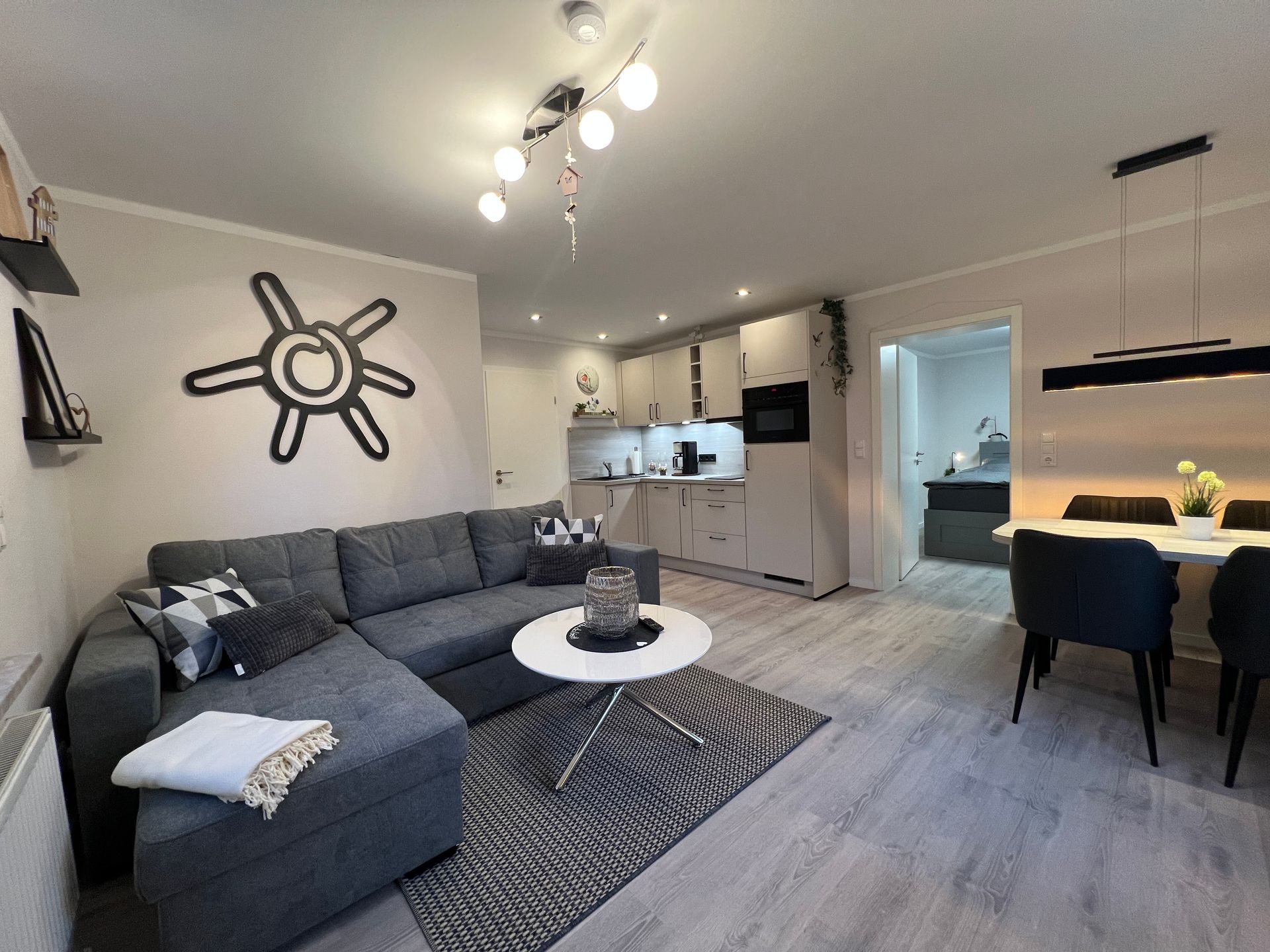 Ein modernes, offenes Wohnzimmer mit grauem Ecksofa, weißem Couchtisch, Küche und Essbereich.
