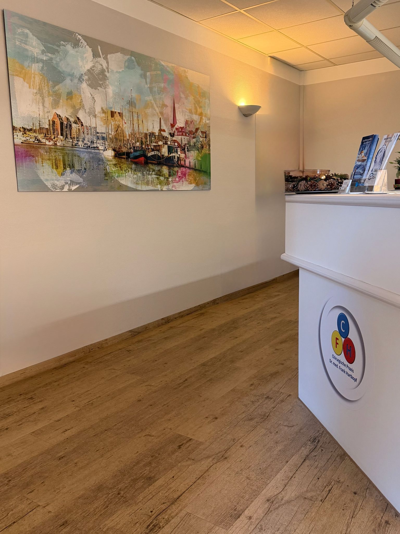 Empfangsbereich mit Gemälde und weißem Schreibtisch mit Logo. Korkboden und weiße Wände.