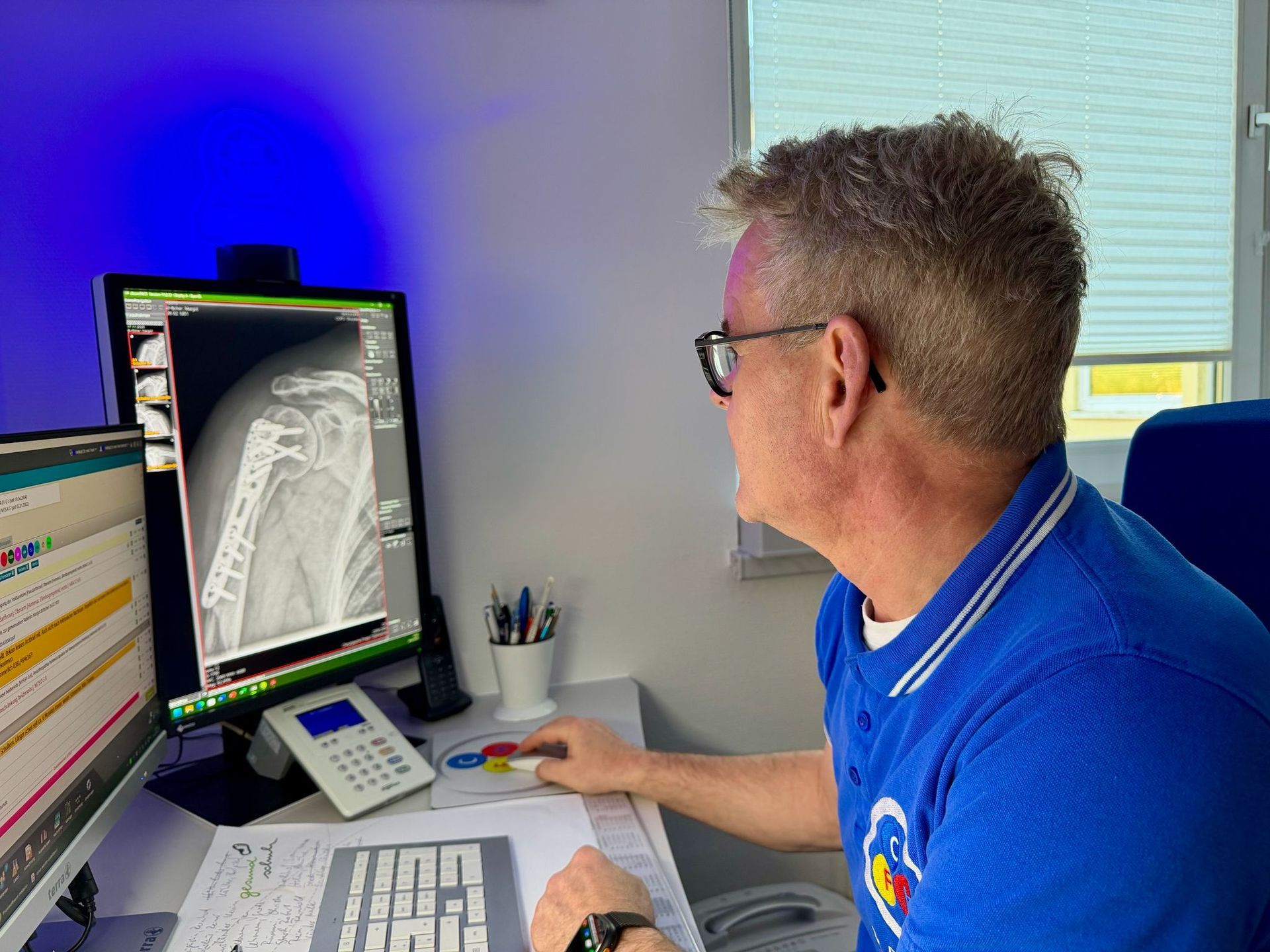 Ein Mann in blauem Hemd betrachtet in einem Büro eine medizinische Röntgenaufnahme auf einem Computerbildschirm.