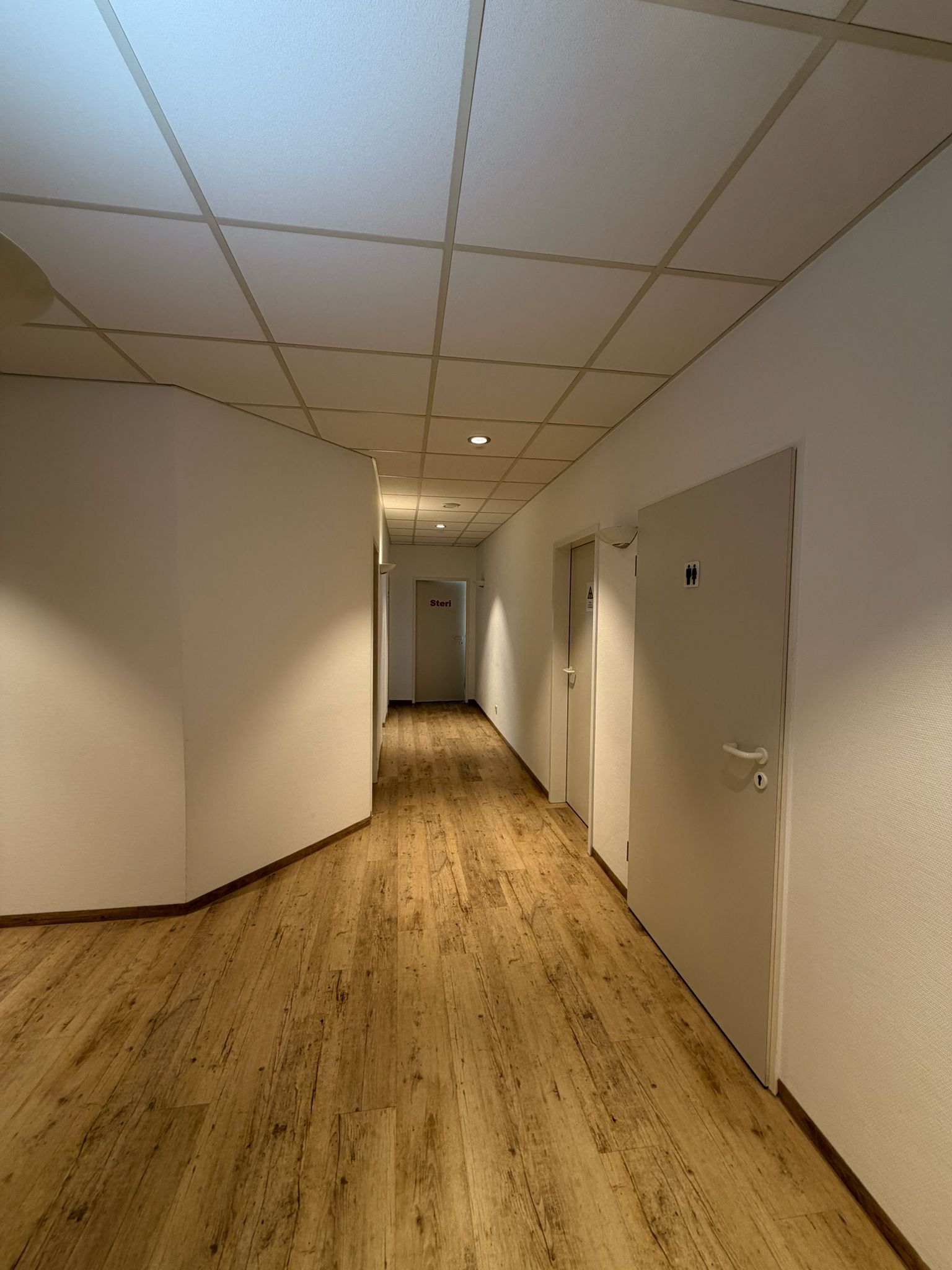 Langer Flur mit hellem Holzboden, weißen Wänden und geschlossenen Türen.