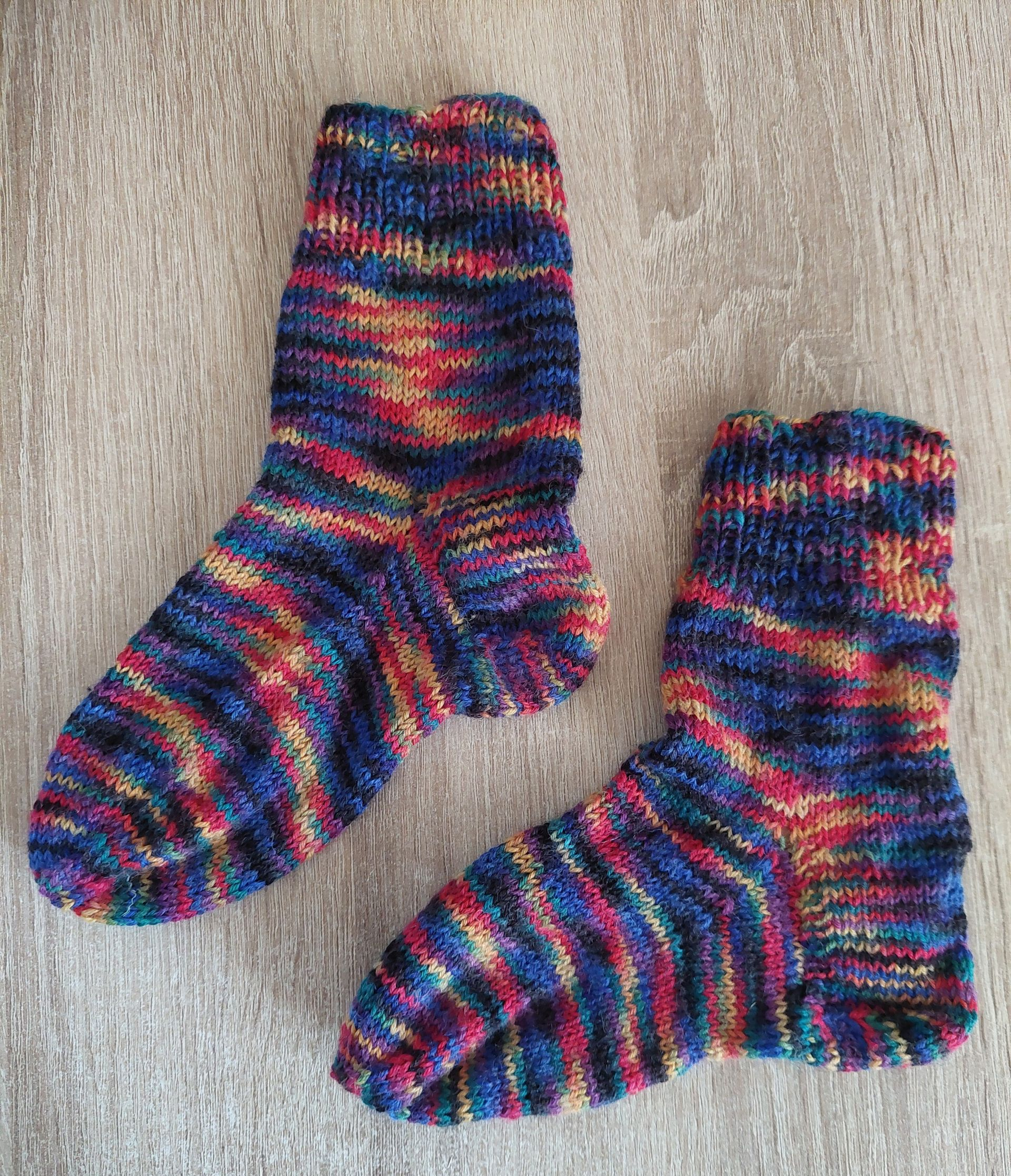 Zwei gestrickte Socken in den Farben Blau, Rot und Gelb liegen auf einer Holzoberfläche.
