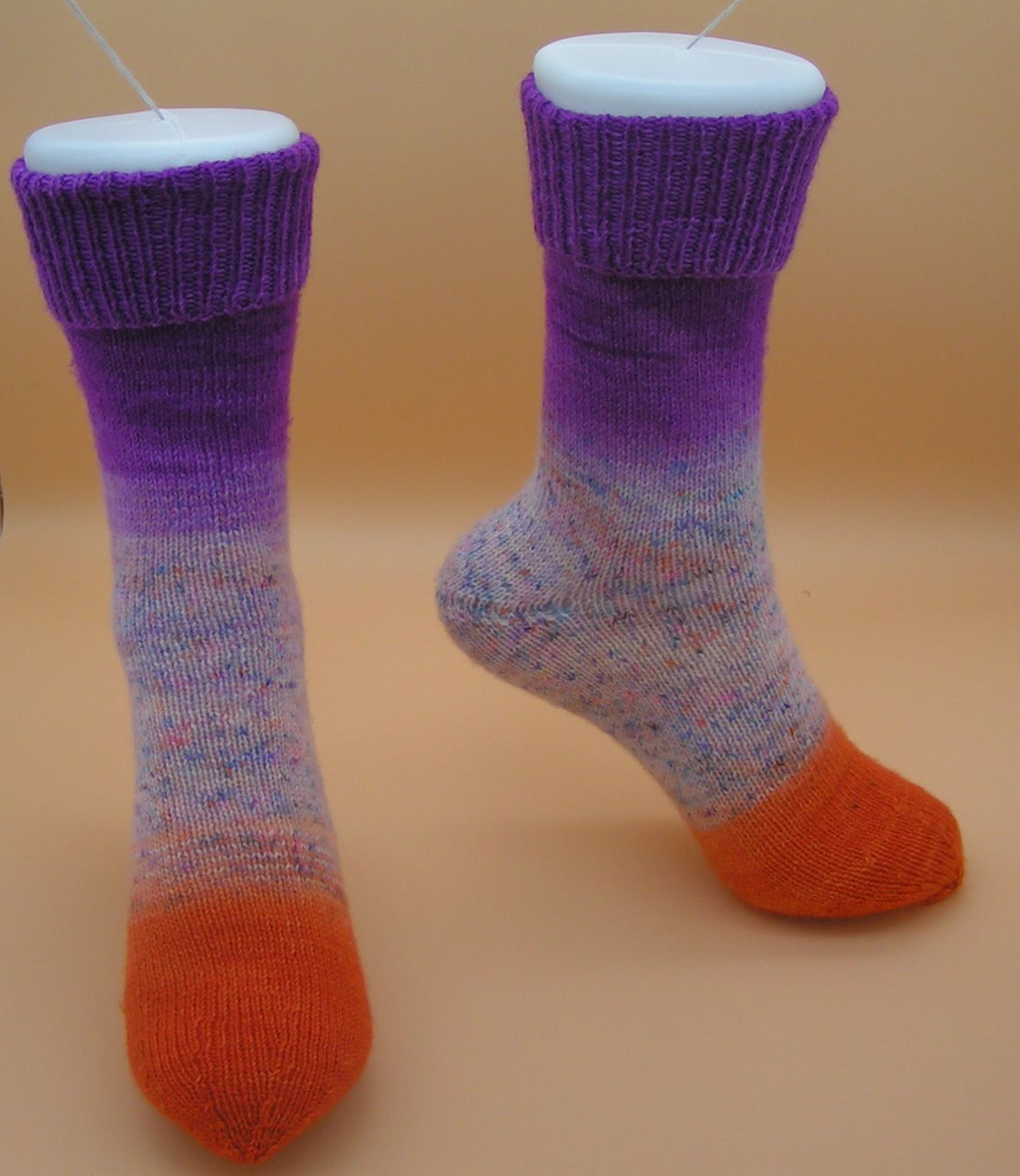 Zwei handgestrickte Socken. Lila Bündchen gehen in einen gesprenkelten Körper über, orange Zehen.