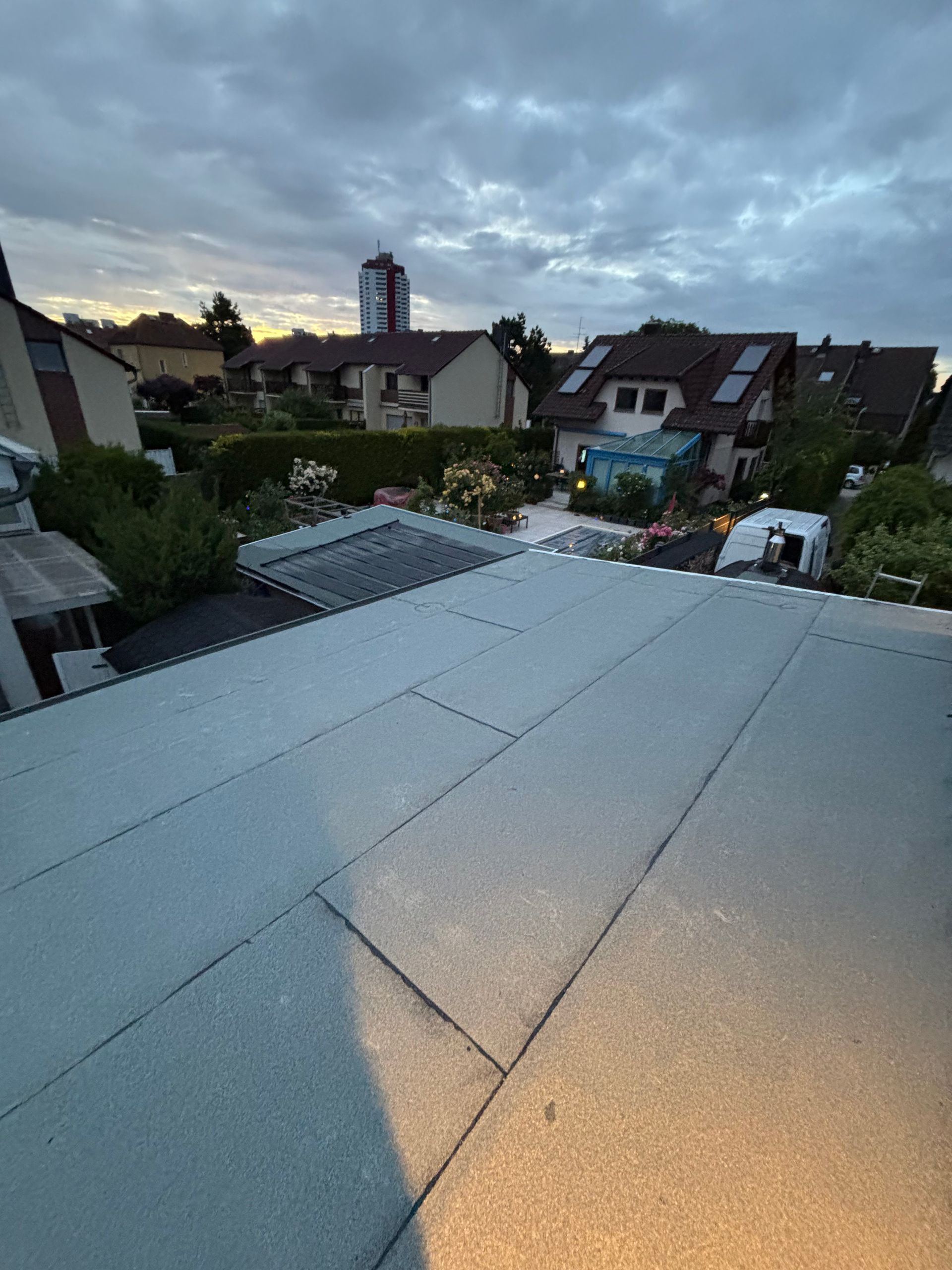 Dachterrasse in der Abenddämmerung mit Blick auf Häuser und Bäume unter einem bewölkten Himmel