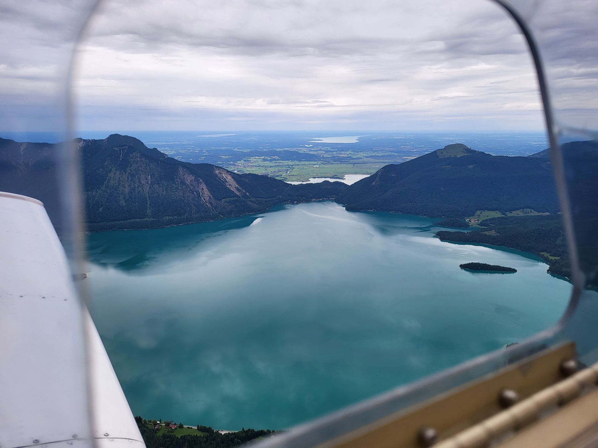 Blick aus einem Flugzeug auf einen Bergsee zwischen bewaldeten Bergen