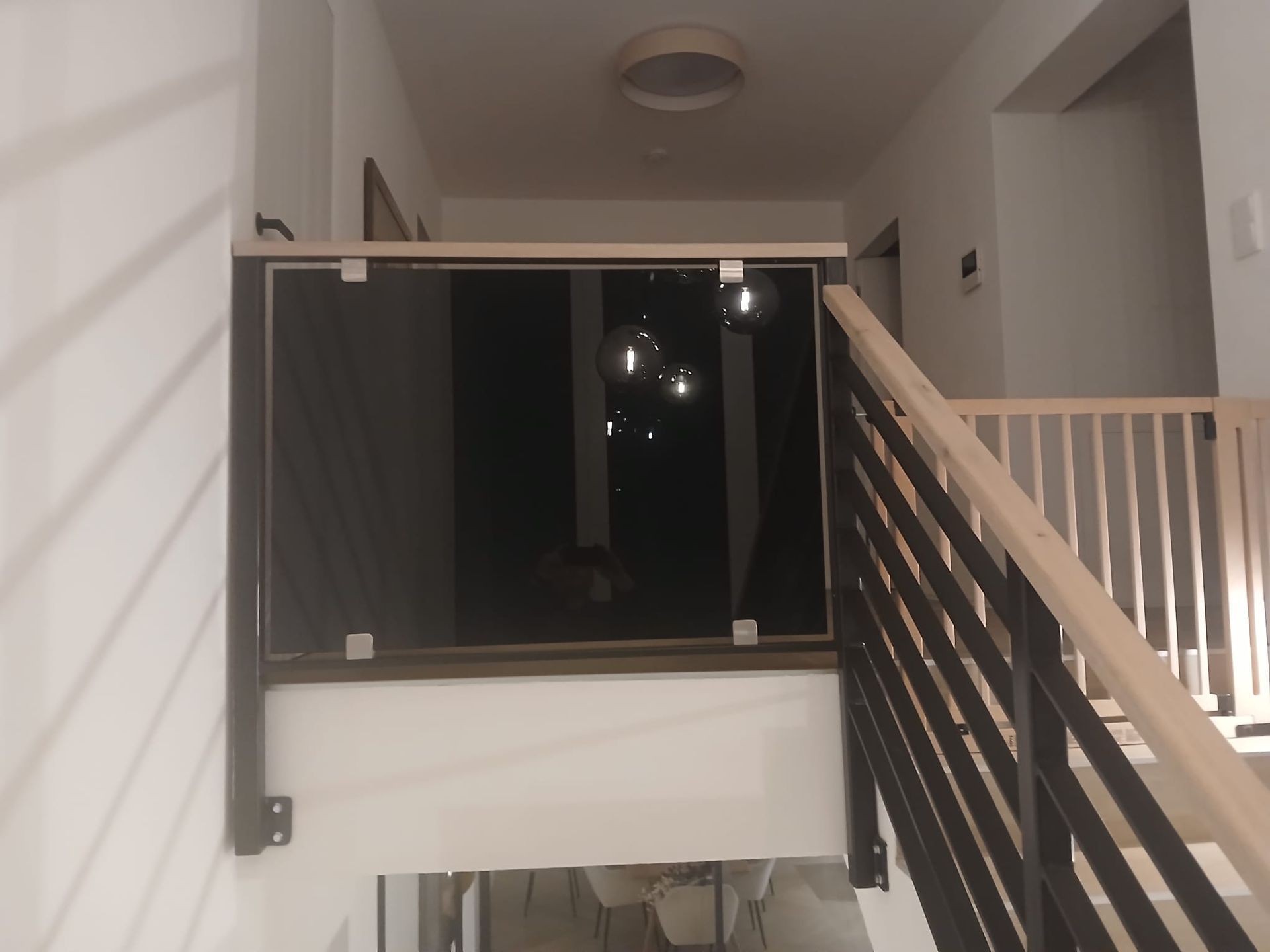 Eine moderne Treppe mit schwarzem und hölzernem Geländer, Glaspaneelen, Flur und Deckenbeleuchtung.