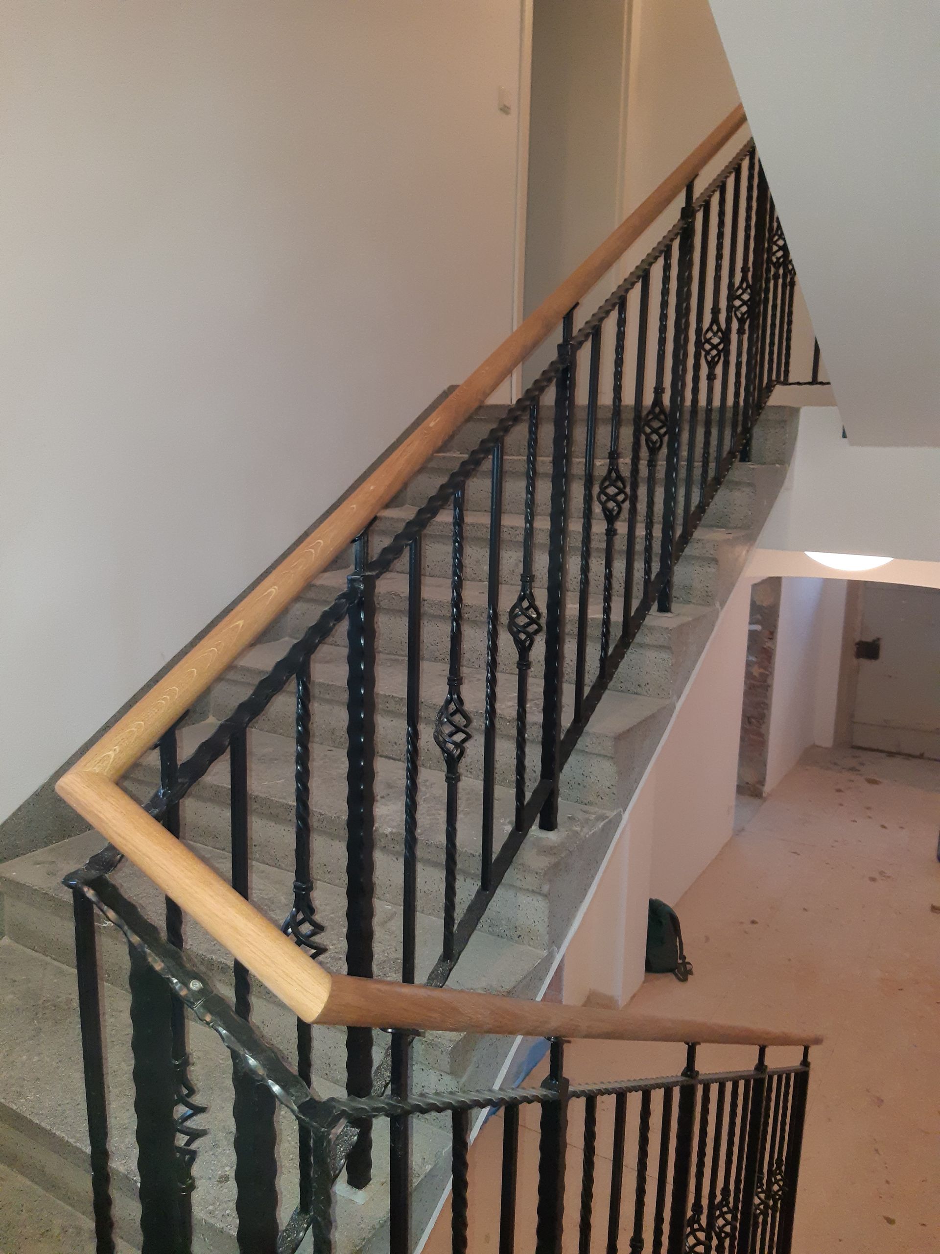 Treppe mit schwarzem schmiedeeisernem Geländer und hölzernem Handlauf, die nach oben führt, in einem Gebäude.