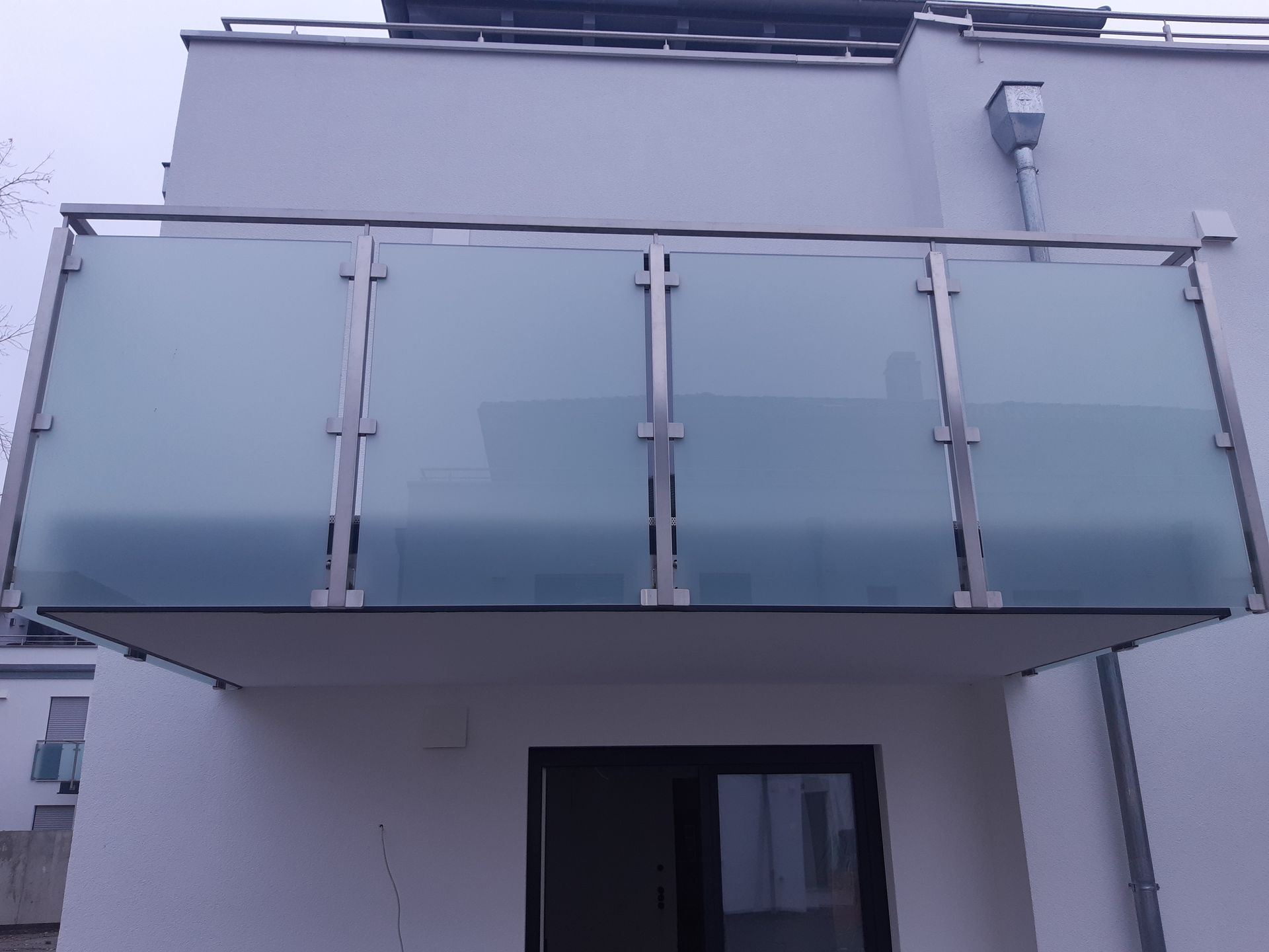 Balkon mit Milchglaspaneelen und Edelstahlrahmen an einer weißen Gebäudefassade.
