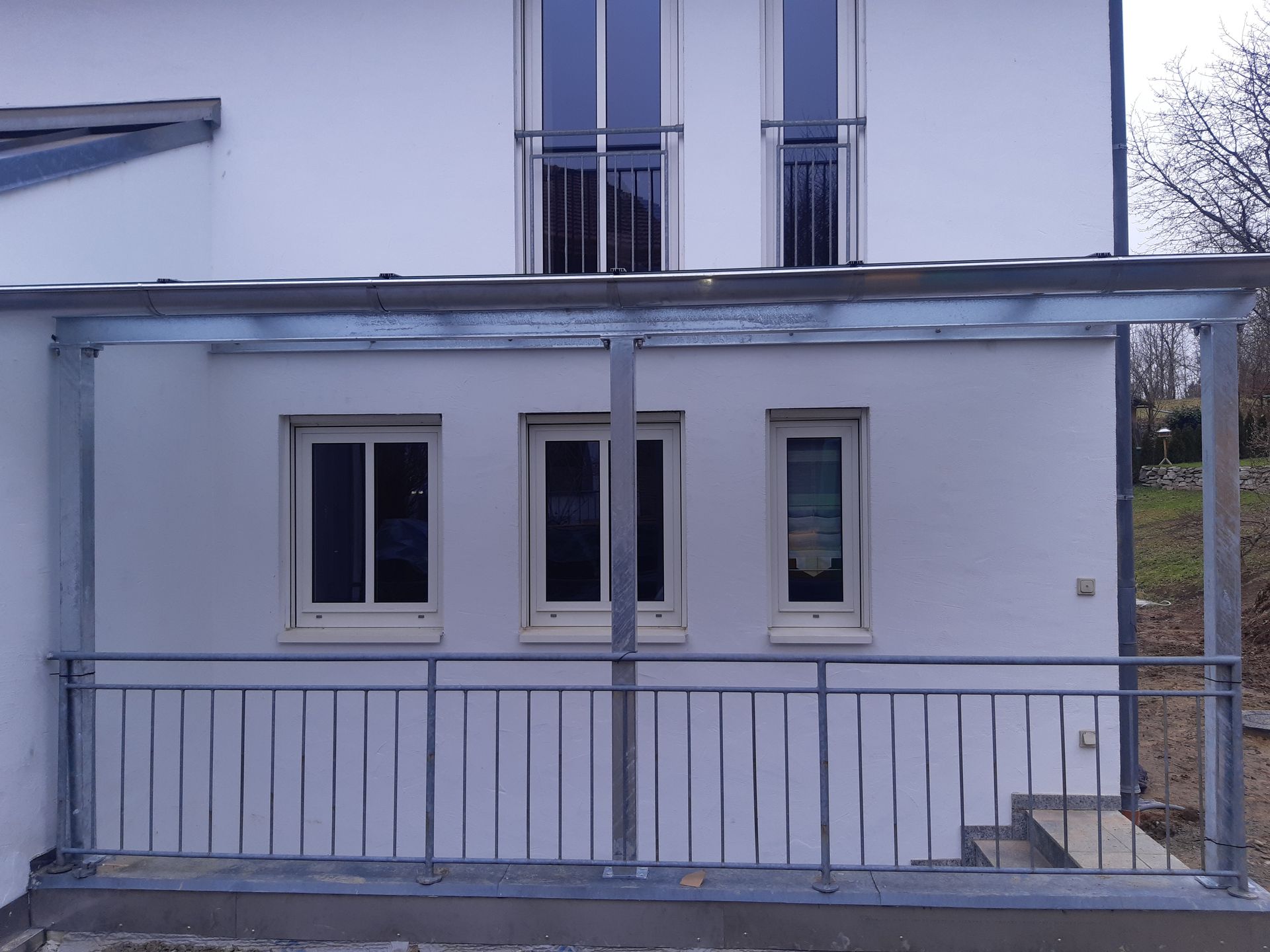 Außenansicht eines weißen Hauses mit Metallveranda und Geländer.