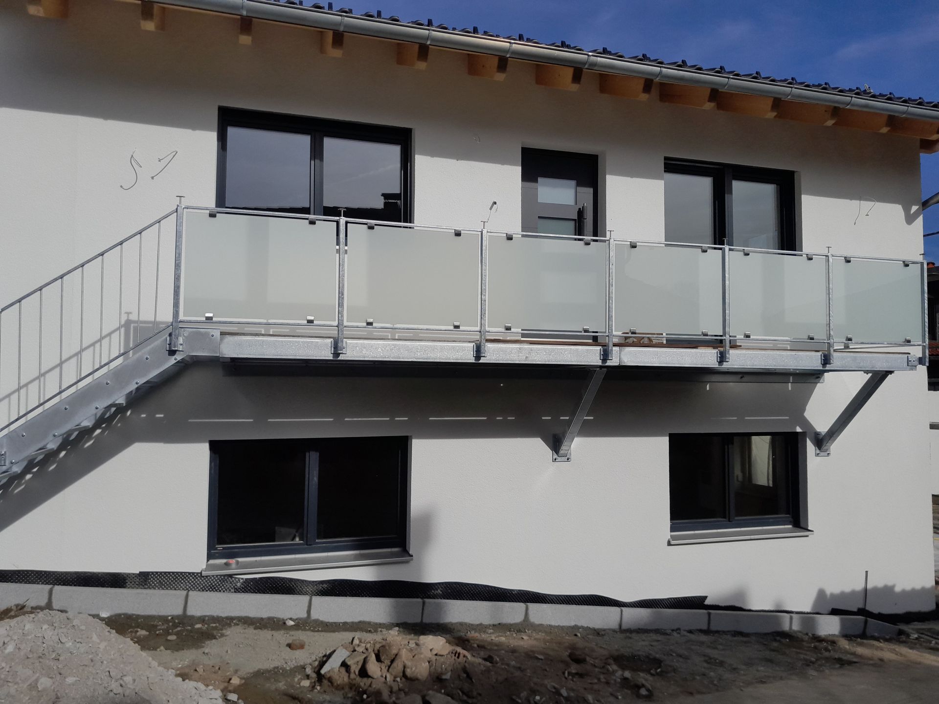 Außenansicht eines zweistöckigen Gebäudes mit Metallbalkon und Treppe.