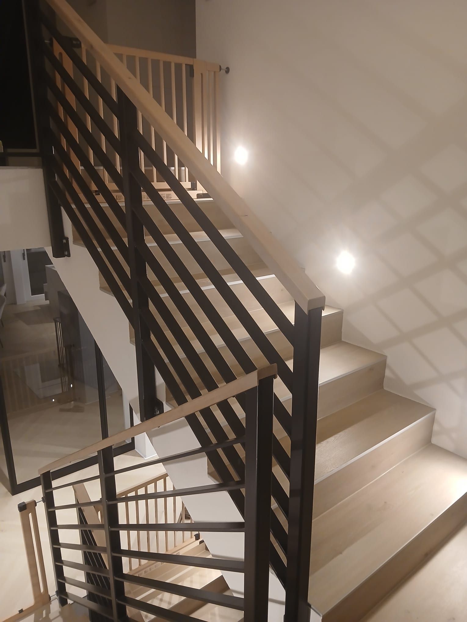 Treppe mit Holzstufen und -geländer, schwarzen Metallstangen und Einbaubeleuchtung.