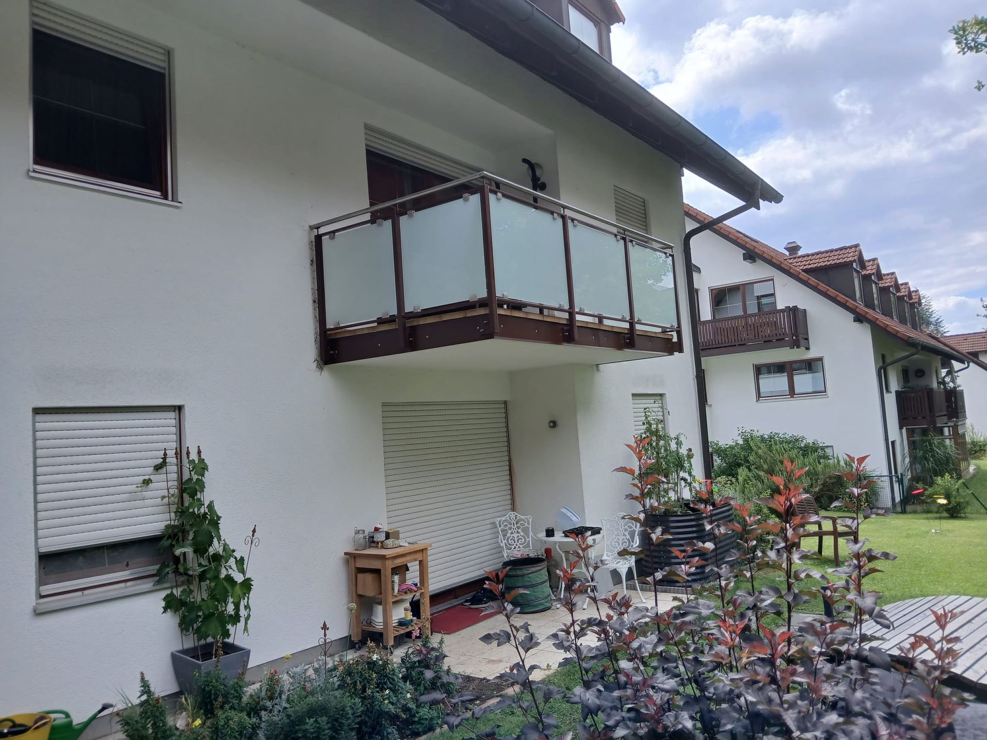 Weißes Gebäude mit Balkon, Glasgeländer und umliegender Landschaftsgestaltung.