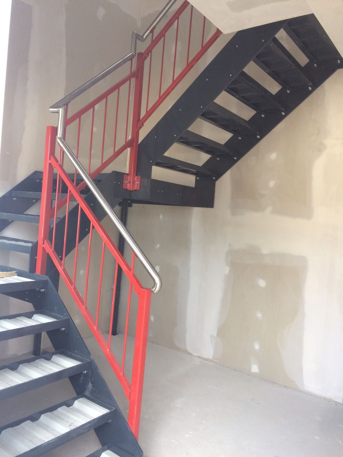 Metalltreppe mit rotem Geländer und schwarzen Stufen in einem Gebäude.