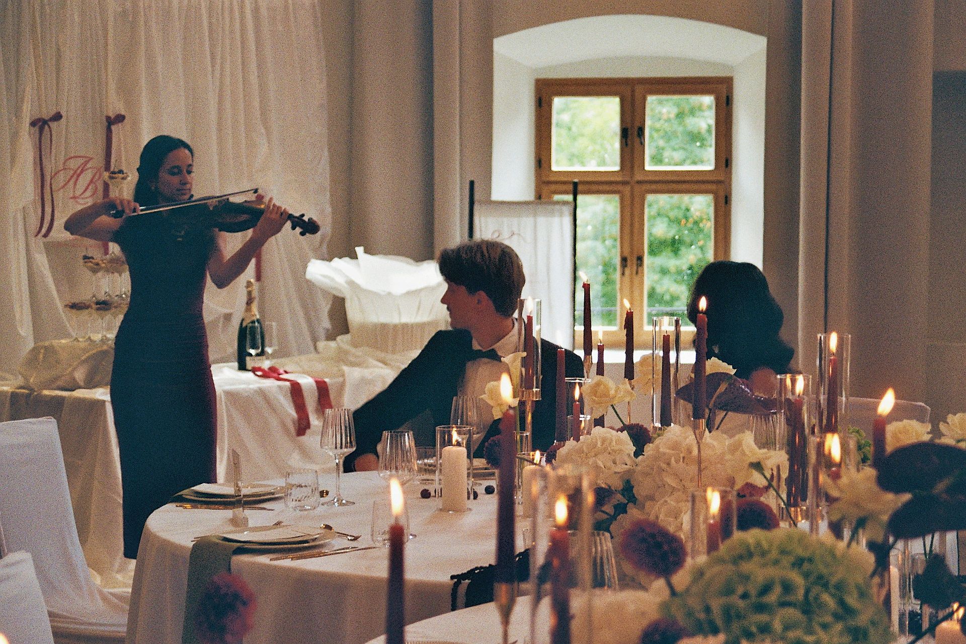 Ein Brautpaar und eine Geigenspielerin sitzen an der Hochzeitstafel.