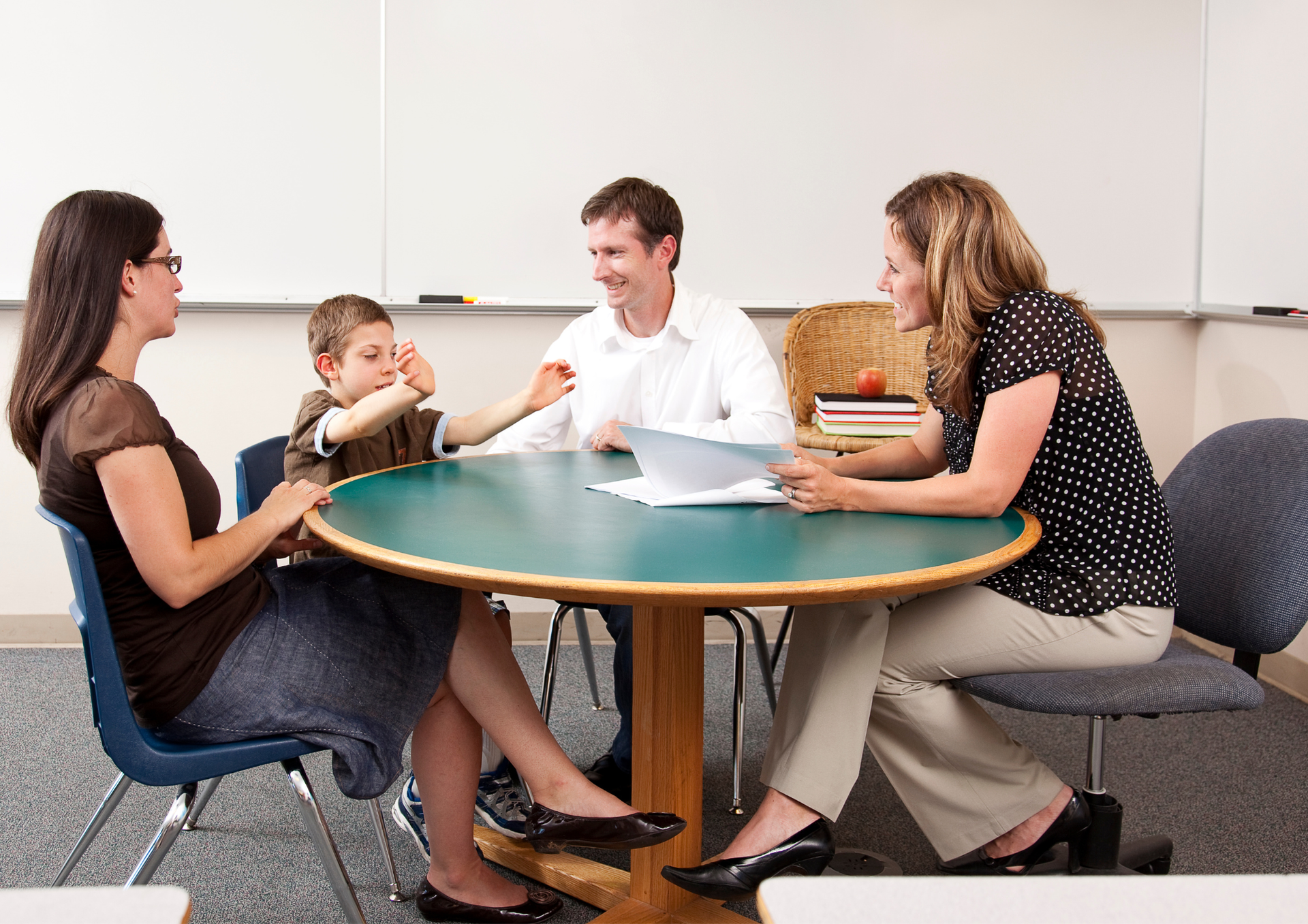 Ein Bild von einem Hilfeplangespräch. Eltern, Betreuer und Kind sitzen an einem runden Tisch. 